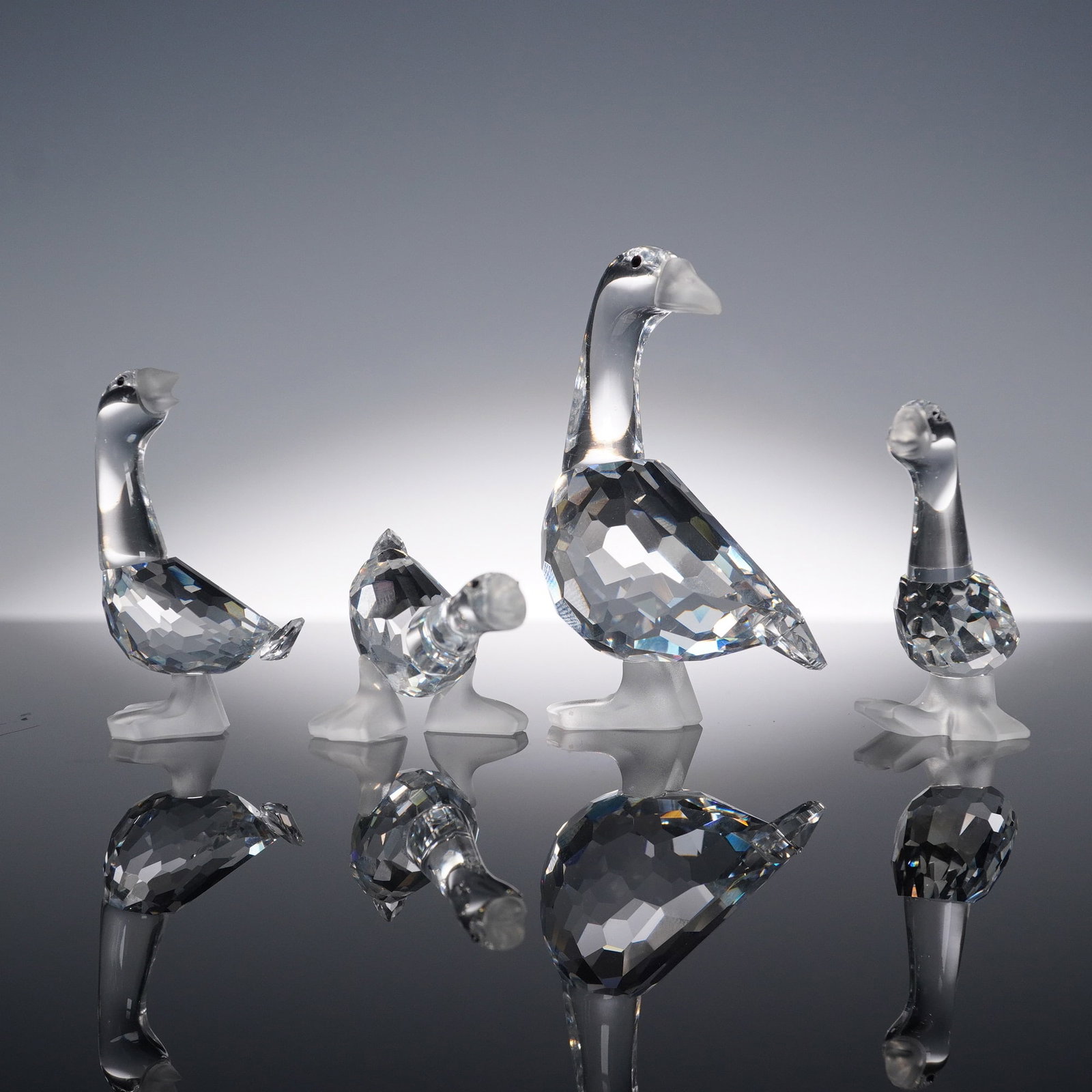 Swarovski Crystal Goose Figurine 4pc Set with Boxes: Swarovski crystal 4pc set of goose figurines featuring a mix of standing and resting poses with faceted clear bodies, frosted beaks, and webbed feet. The group includes one large goose and three small