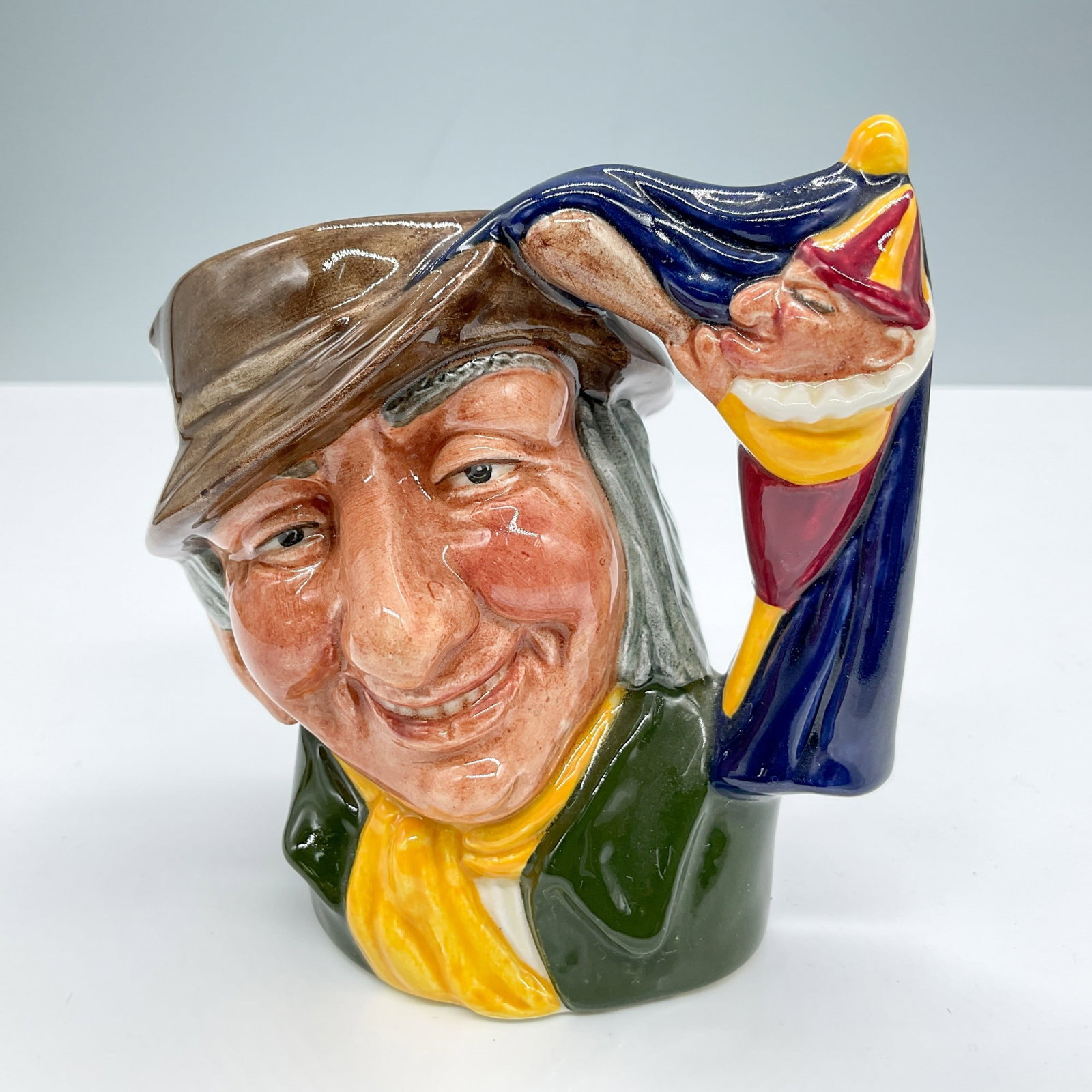Punch and Judy Man D6593 Small Royal Doulton Character Jug: Brown hat; green coat; yellow scarf. Royal Doulton backstamp. Artist: David B. Biggs Issued: 1964 - 1969 Dimensions: 3.5"H Country of Origin: England