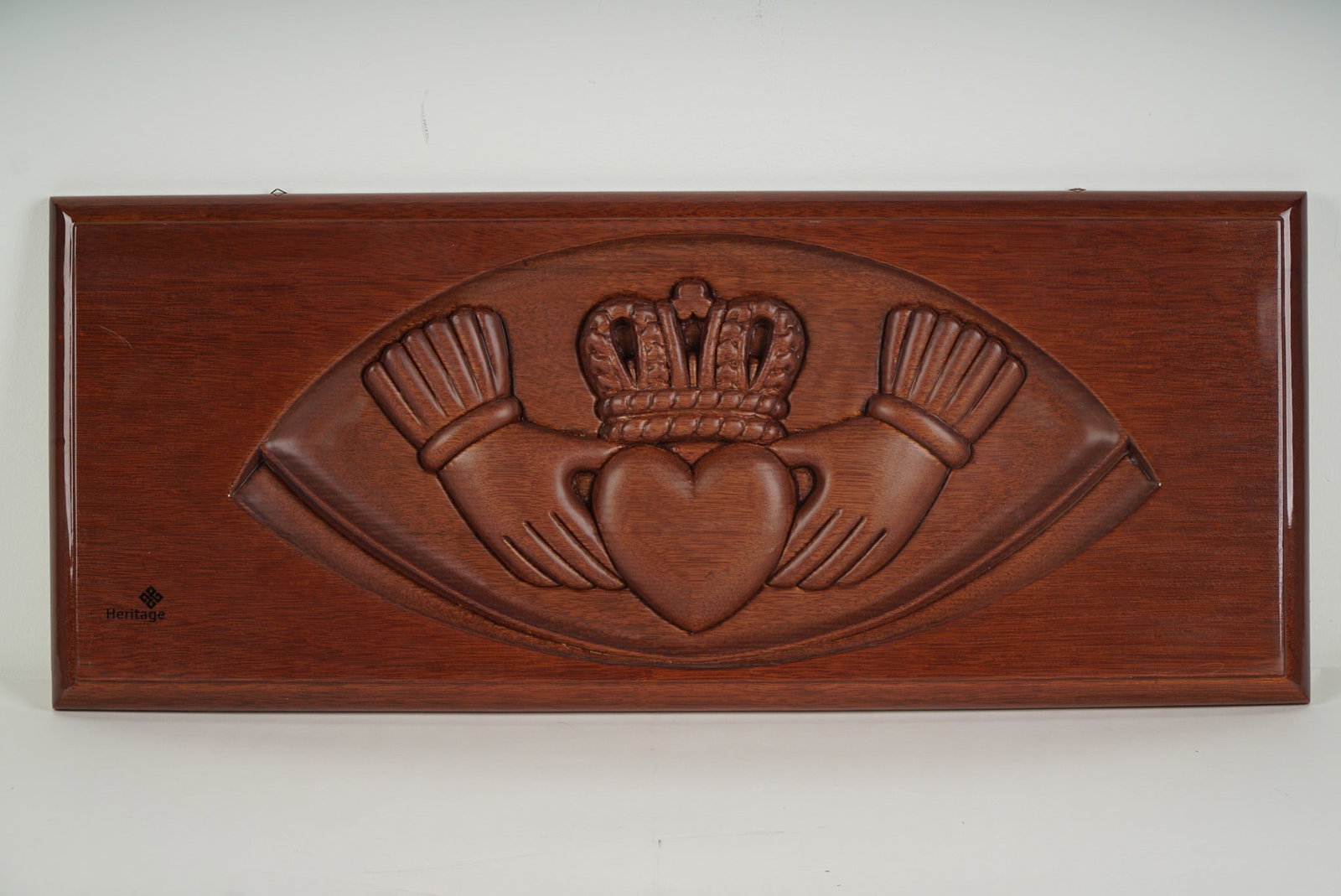 Heritage Hand-Carved Mahogany Wall Panel, Claddagh Symbol: Heritage mahogany wall panel intricately hand-carved with the traditional Irish Claddagh motif, symbolizing love, loyalty, and friendship. The central design features two hands cradling a heart topped
