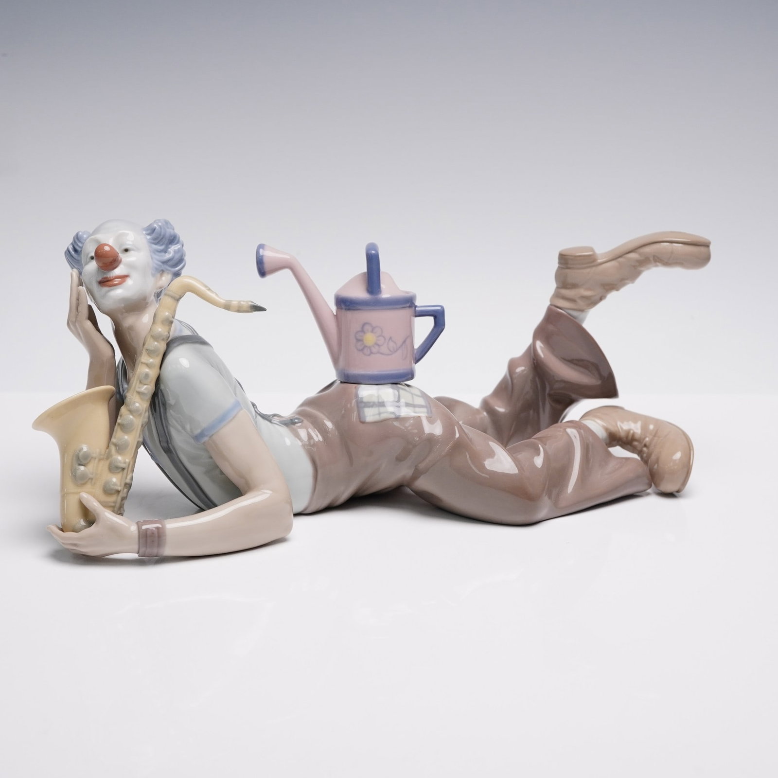 Lladro Porcelain Figurine, Seeds of Laughter 1005764: Porcelain figurine titled Seeds of Laughter by Lladro, model number 1005764. Sculpted by Salvador Furio and issued in 1991, this whimsical clown lounges on the ground, cradling a saxophone with a wate