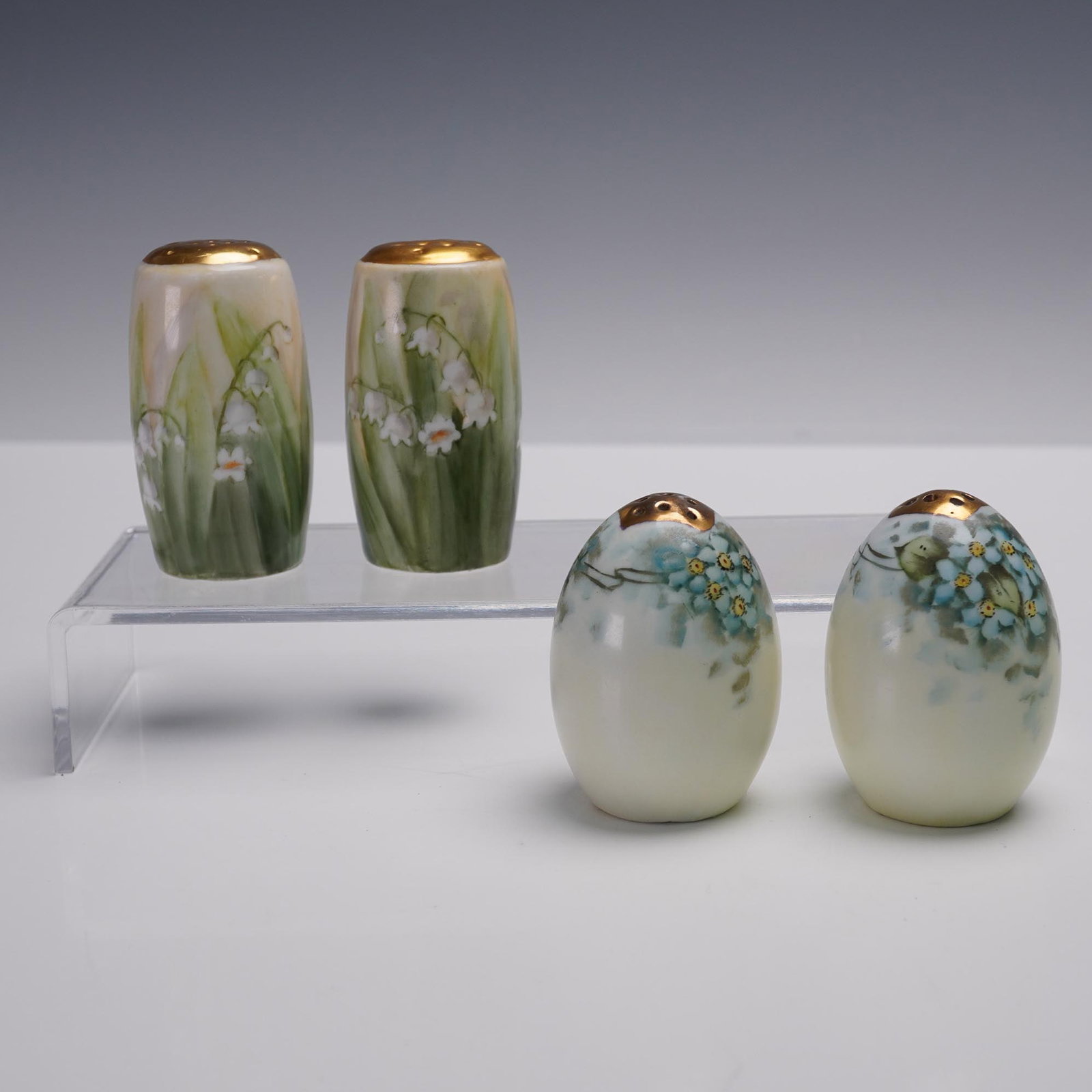 2 Pairs of Bavarian Porcelain Salt and Pepper Shakers: This auction lot includes two pairs of Bavarian porcelain salt and pepper shakers, each meticulously hand-painted with delicate floral motifs. The first pair is adorned with a beautiful depiction of l