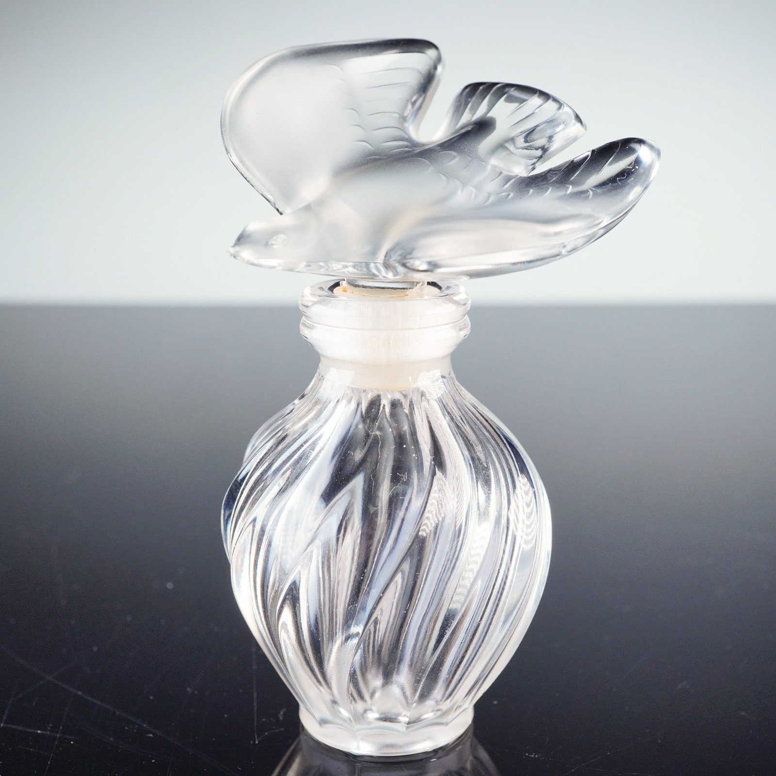 Lalique for Nina Ricci Crystal Perfume Bottle, L'Air du Temps: Lalique for Nina Ricci crystal perfume bottle, L'Air du Temps, featuring a frosted and clear glass dove stopper and a fluted swirl body design. This elegant collectible showcases the signature craftsm
