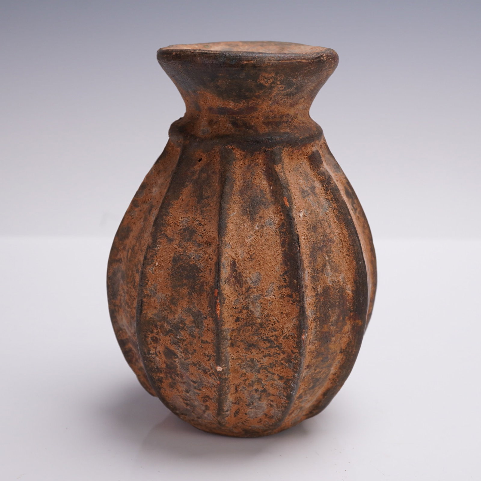 Pre-Columbian-Style Carinated Terracotta Vessel, Possibly Poison Jar: A striking Pre-Columbian carved terracotta jar featuring a deeply ridged melon-form body and short flared neck, its surface covered in a rich earthen patina of orange and black mineral deposits. This 