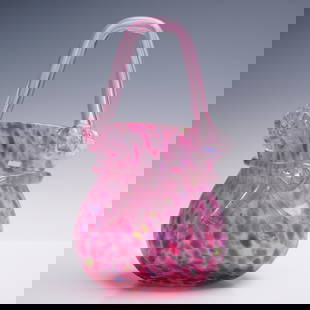 Hand-Blown Art Glass Vase in Pink Confetti with Applied Handle: A vibrant hand-blown art glass vase in the shape of a stylized purse, standing 9 inches tall. This playful, sculptural form features a mottled "confetti" pattern in bright pink with splashes of green,