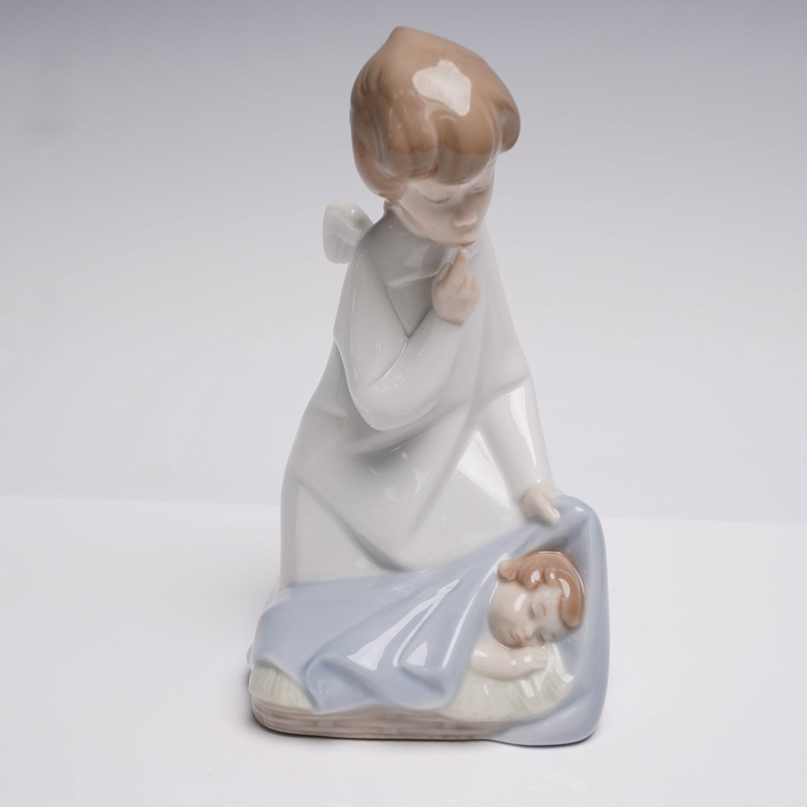 Lladro Porcelain Figurine, Angel with Child 1004635: Lladro porcelain figurine titled Angel with Child, model number 1004635, depicting an angel in a white robe kneeling beside a sleeping child covered with a blue blanket. Designed in a delicate pastel