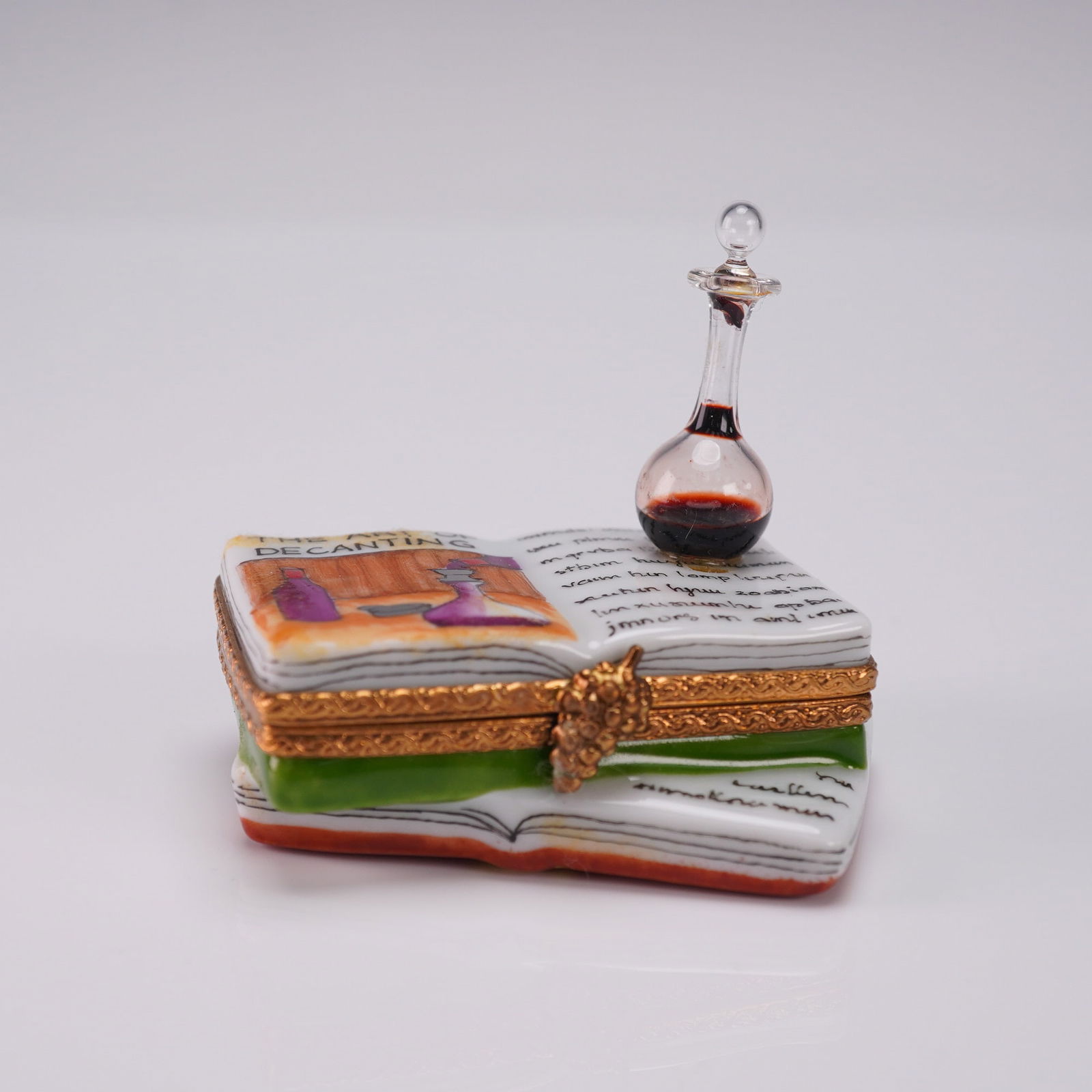 Limoges France Ring Box Art of the Wine with Mini Decanter: Limoges France hand-painted porcelain ring box shaped like an open book titled Art of the Wine, decorated with wine-themed illustrations and a grapevine clasp. Includes a tiny glass decanter accessory