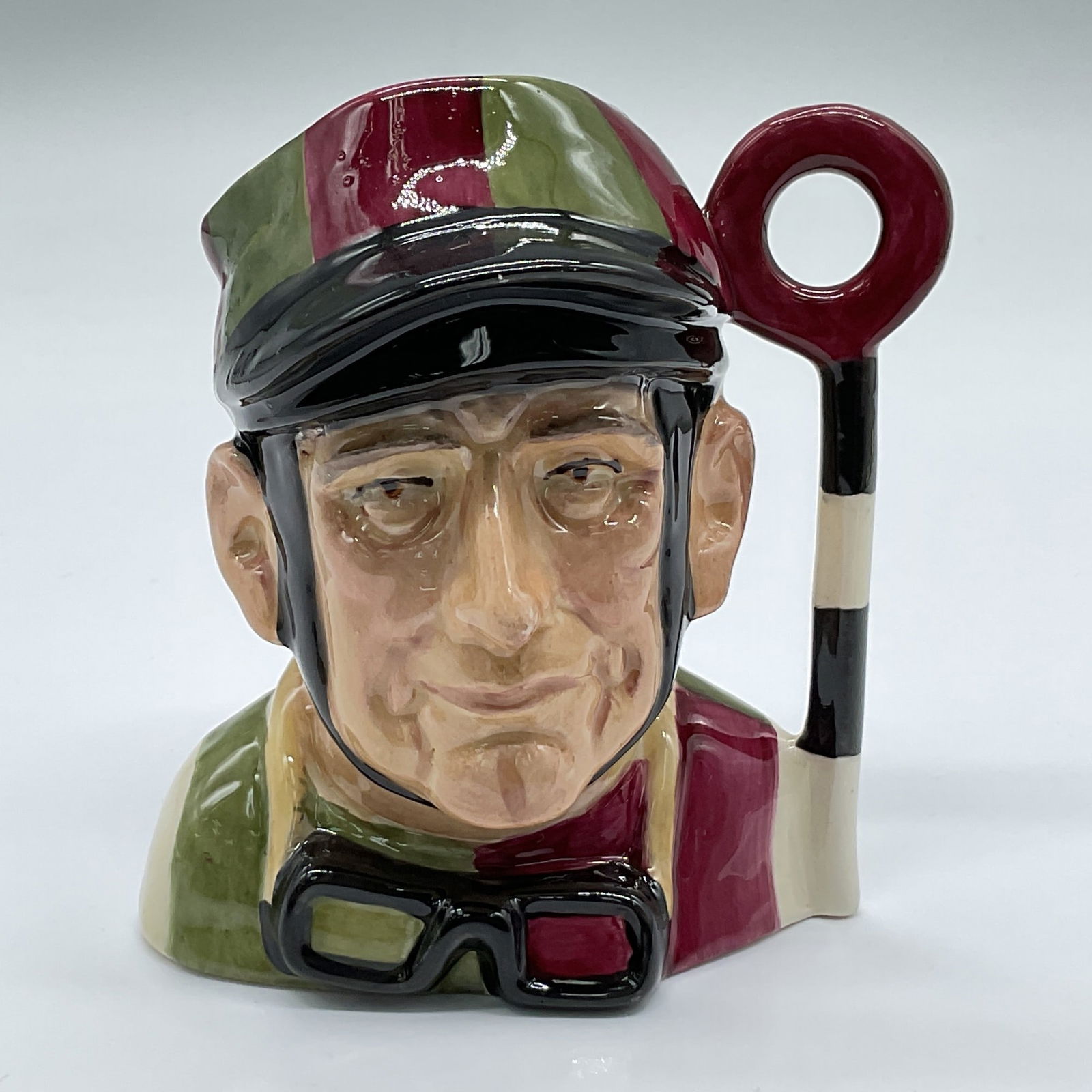 Royal Doulton Prototype Colorway Character Jug, Jockey: D6629. First version. Hand painted medium figural jug of a horse-rider in a maroon and green jacket and cap. Winning pole handle. Royal Doulton backstamp. Artist: David B. Biggs Issued: 1970s Dimensio