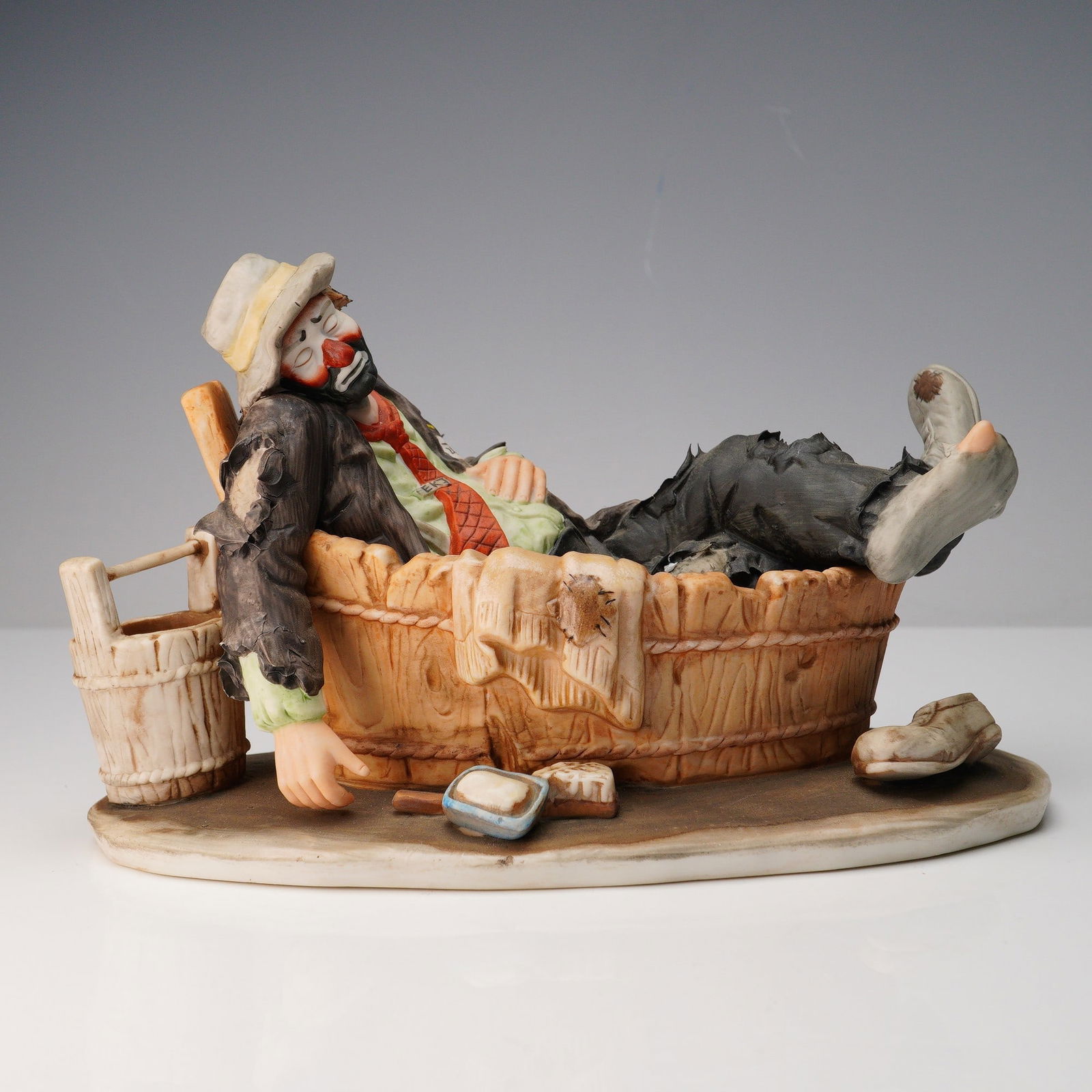 Emmett Kelly Jr Porcelain Figurine, Saturday Night: Bisque porcelain figurine titled Saturday Night, featuring Emmett Kelly Jr's iconic "Weary Willie" character reclining in a wooden washtub with an exhausted demeanor, his signature red nose and sad ex