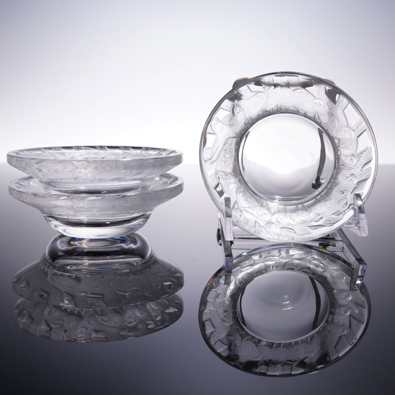 3pc Lalique Crystal Irene Ashtrays France: Set of three Lalique crystal ashtrays in the Irene pattern, featuring a raised border of birds in flight. Each piece is signed Lalique France on the base. Measures approximately 3.5" dia. Dimensions: 