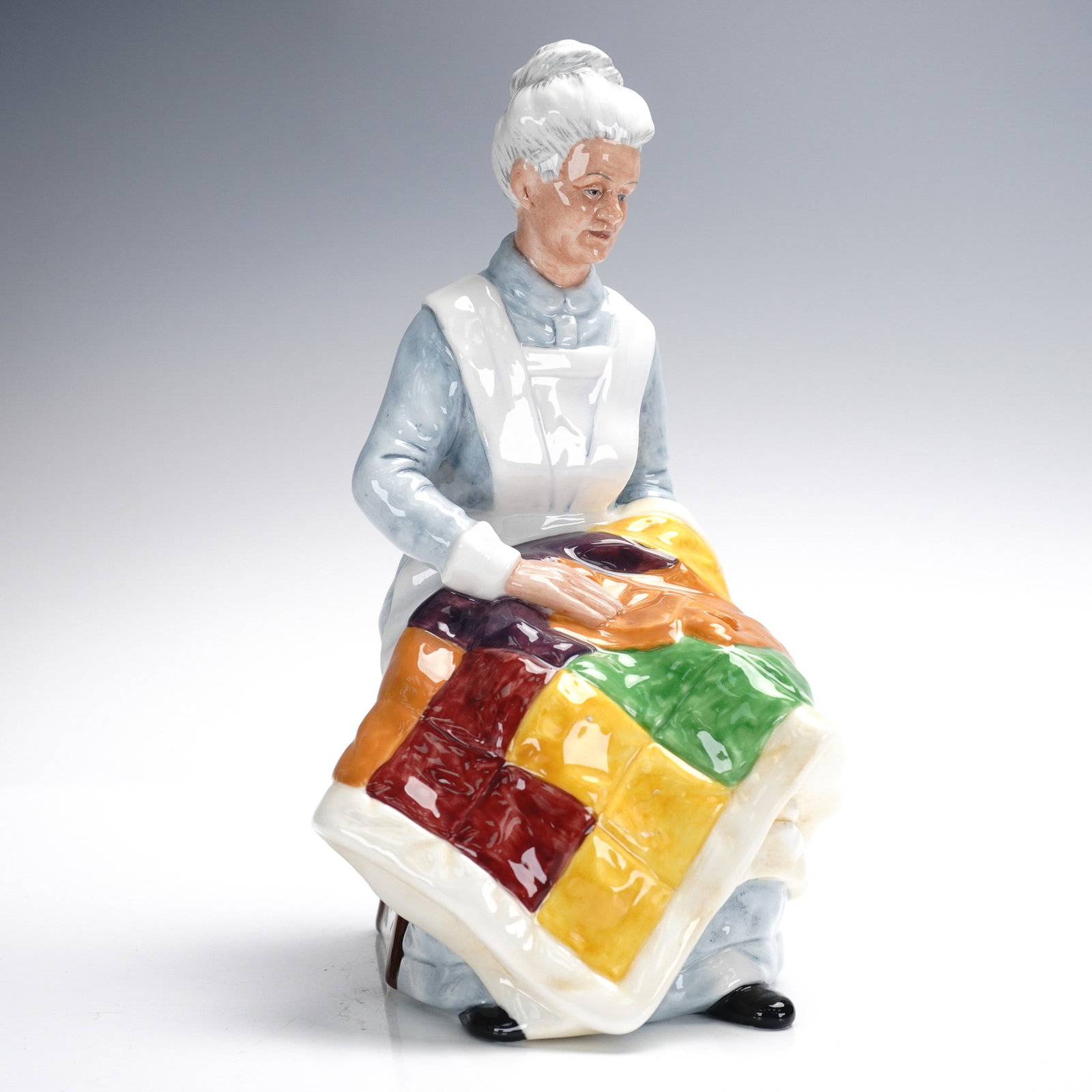Royal Doulton Figurine, Eventide HN2814: Royal Doulton figurine titled Eventide, model HN2814, portraying an elderly woman seated as she hand-stitches a colorful patchwork quilt. This collectible was designed by artist Adrian Hughes and is m
