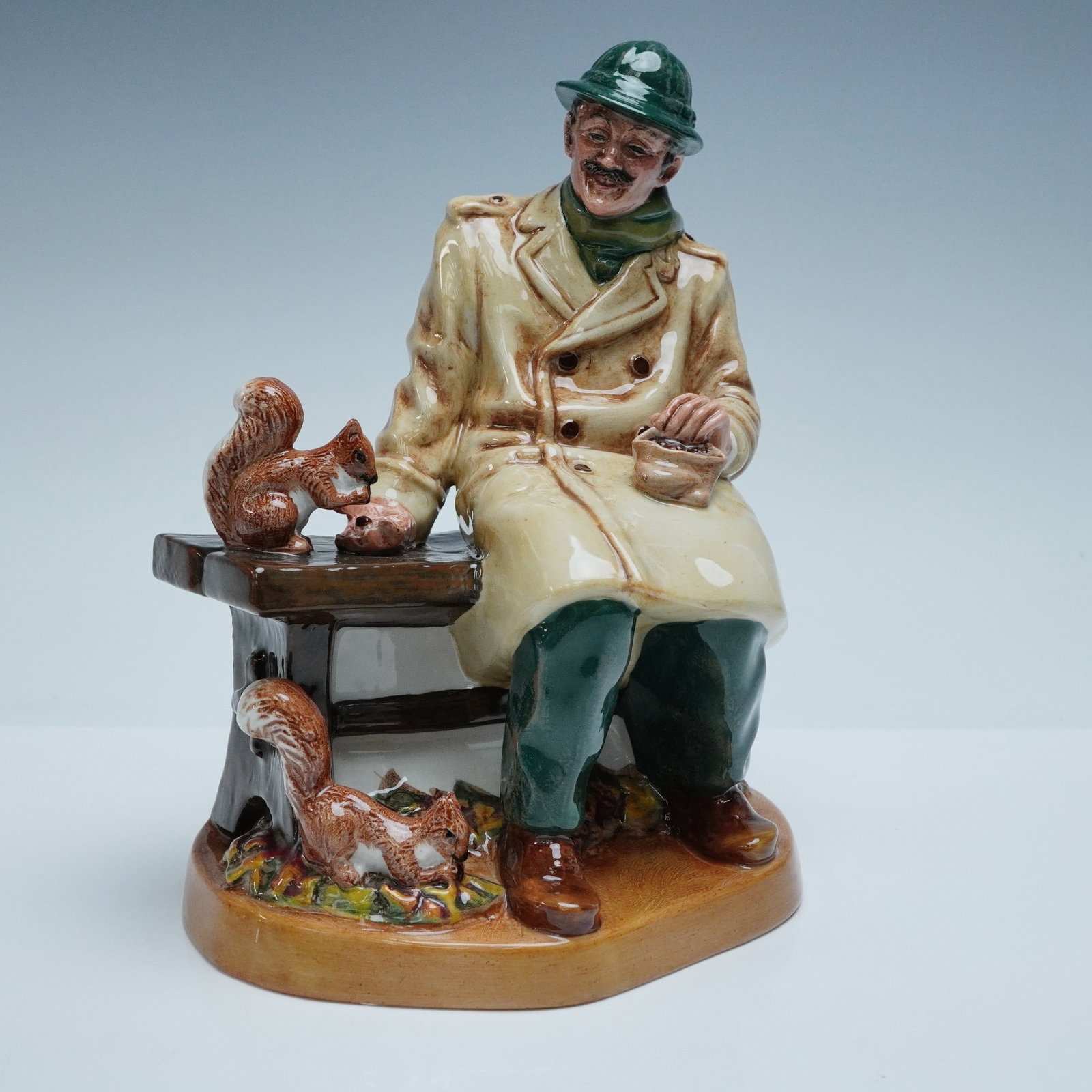 Royal Doulton Figurine, Lunchtime HN2485: Royal Doulton figurine titled "Lunchtime," model HN2485. This hand-painted porcelain figure depicts a cheerful man seated on a bench feeding squirrels. Royal Doulton backstamp with HN number. Artist: 