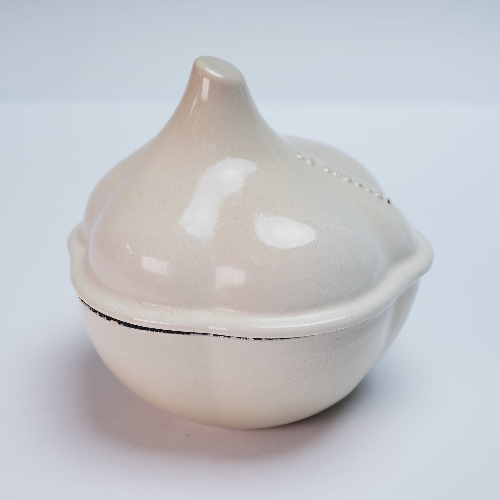 Le Creuset Cast Iron Mini Garlic Cocotte: Le Creuset cast iron mini garlic cocotte in a soft cream meringue glaze, featuring a sculptural bulb-shaped design with embossed Le Creuset lettering on the lid. This enameled stoneware dish is ideal 