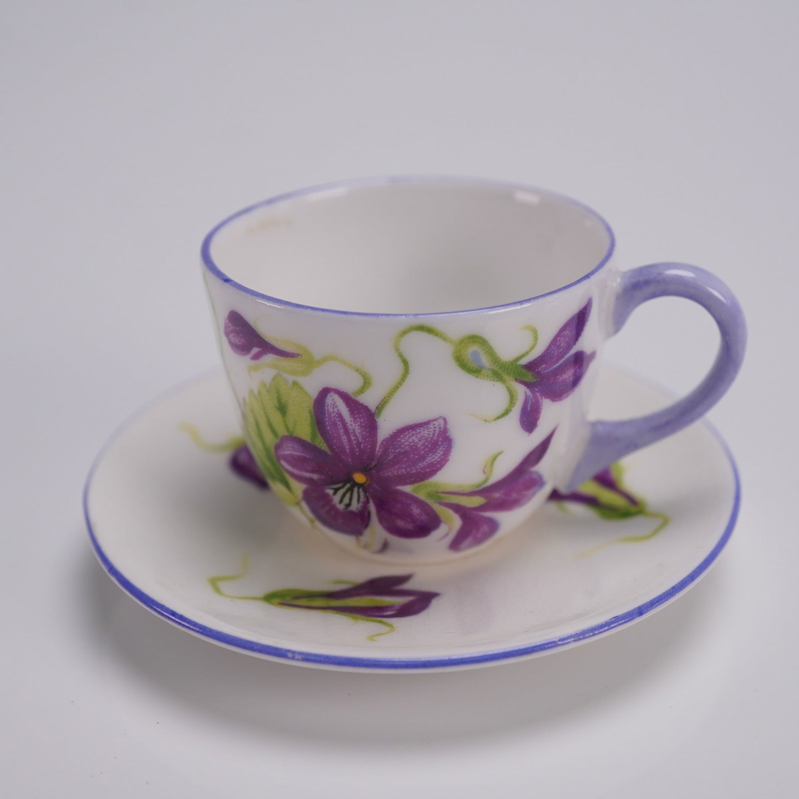 2pc Shelley Miniature Demitasse Cup and Saucer, Violets Dainty: Shelley fine bone china toy-sized demitasse cup and saucer in the Dainty shape, decorated in the Violets pattern. The cup features a gently flared form with a soft lilac handle and rim, adorned with d
