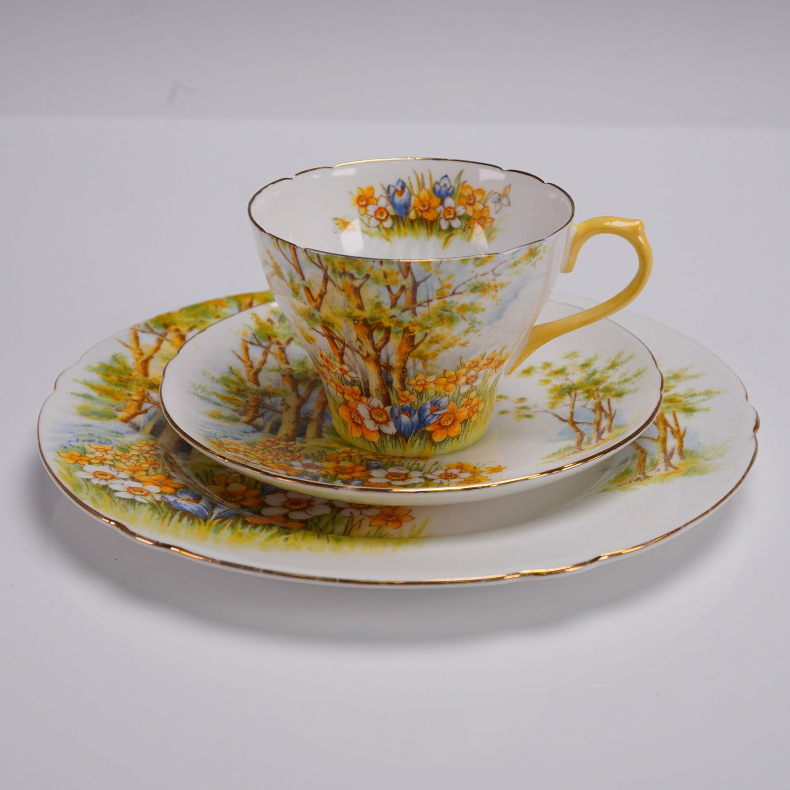 3pc Shelley Fine Bone China Tea Trio Daffodil Time Pattern: Shelley England fine bone china tea trio in the Daffodil Time pattern. This 3-piece set features a vivid springtime landscape with blooming daffodils and trees, accented with gold trim. Includes one t
