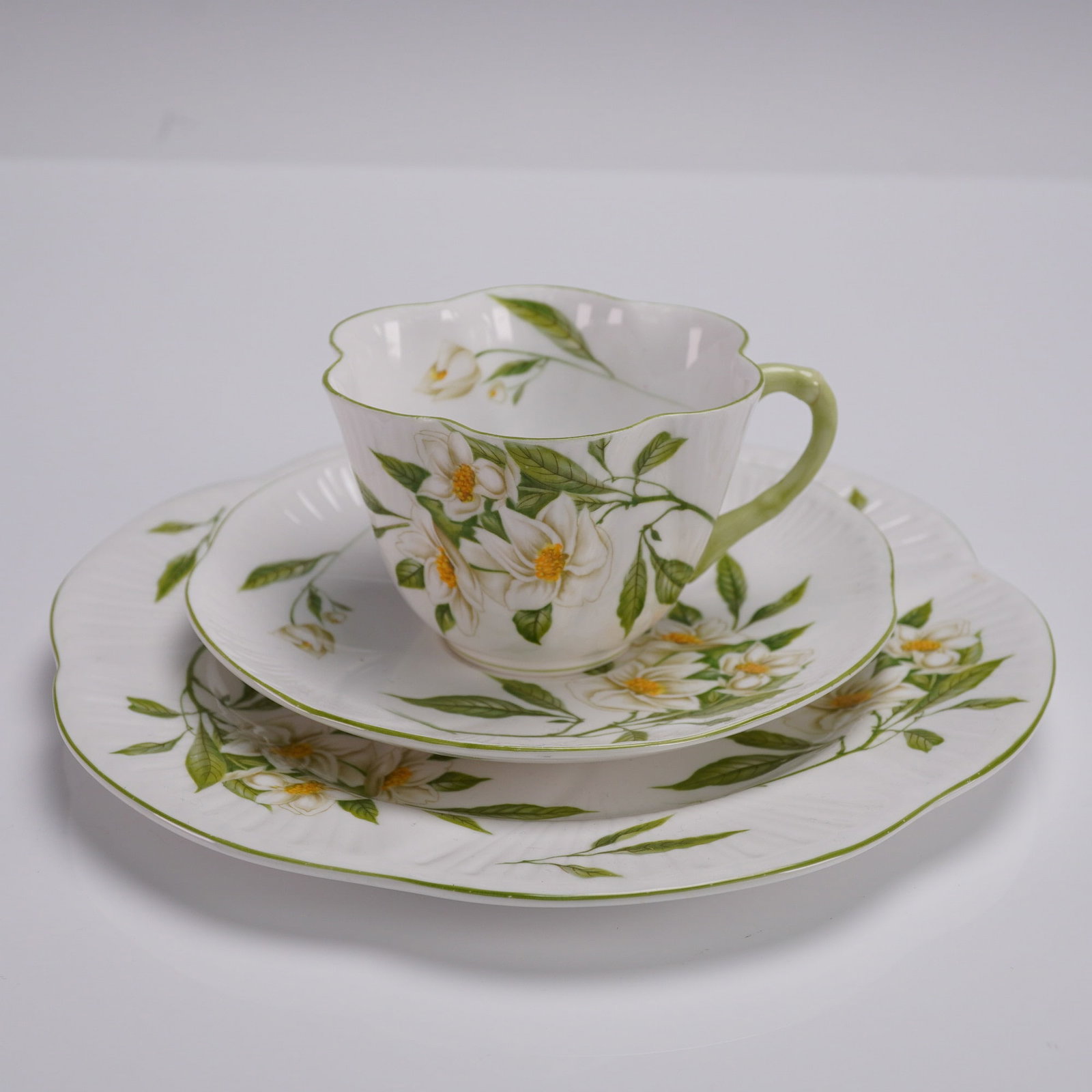 3pc Shelley Fine Bone China Teacup Set Syringa Pattern England: 3 piece Shelley fine bone china teacup set in the Syringa pattern, Dainty shape with green trim. The set includes a scalloped teacup with green handle, matching saucer, and salad plate, all featuring 