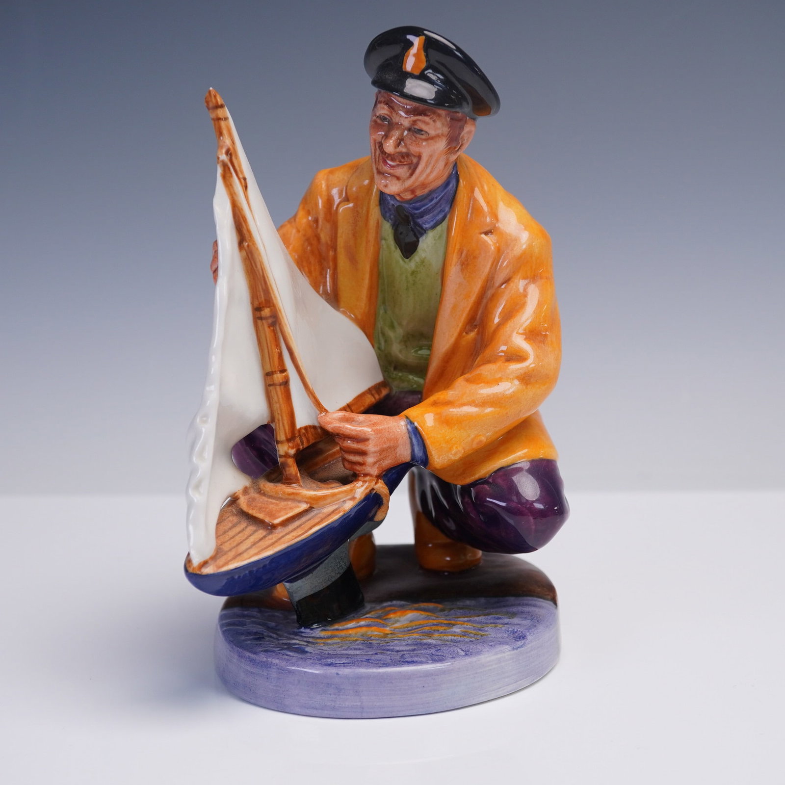 Royal Doulton Porcelain Figurine, Sailor's Holiday HN2442: From Royal Doulton's character figure collection, Sailor's Holiday HN2442 depicts a cheerful sailor crouched down to prepare his toy sailboat for launch, captured in vibrant hand-painted detail. Issue