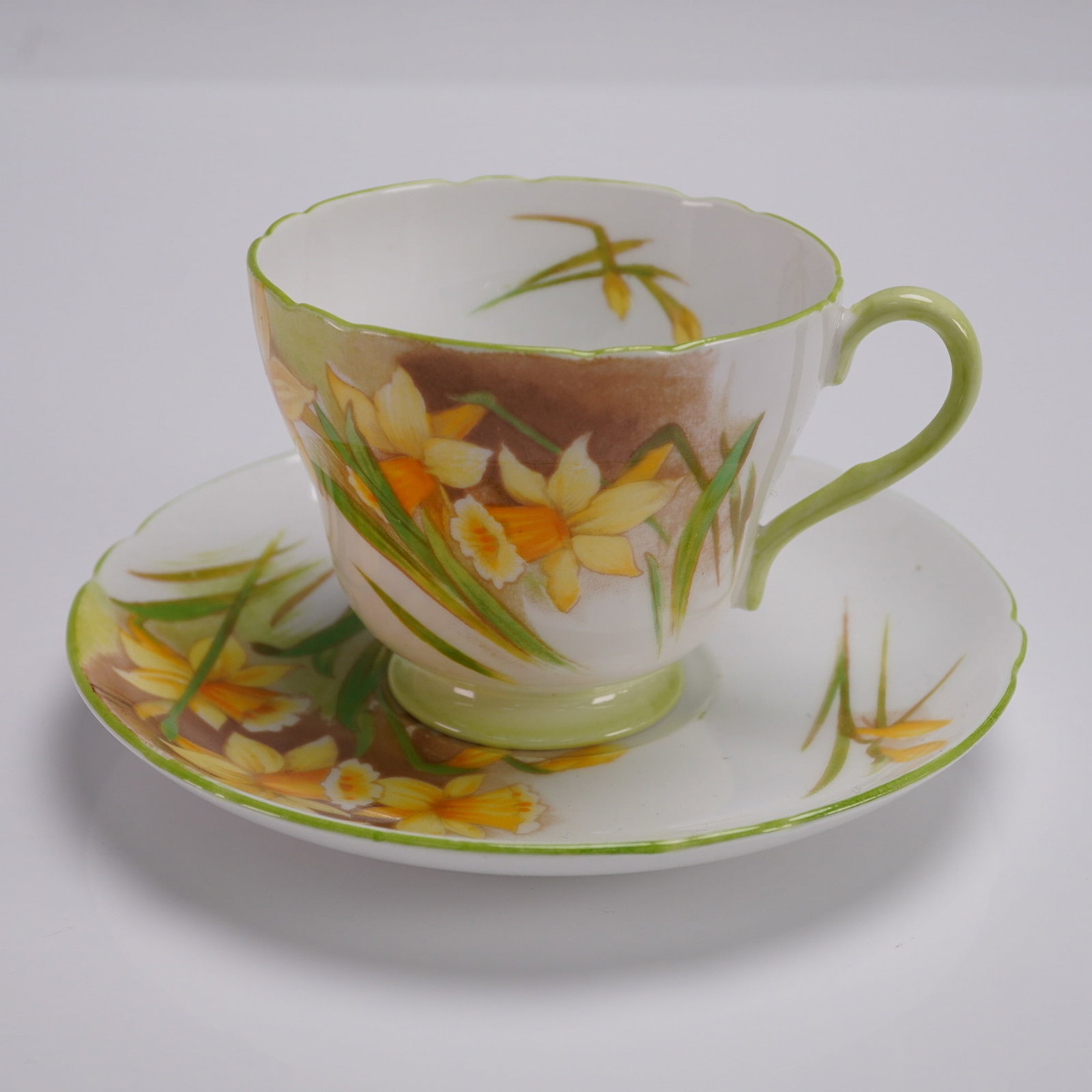 2pc Shelley Fine Bone China Teacup Set Daffodil Pattern 13670: Shelley England fine bone china teacup and saucer set in pattern number 13670, featuring hand-painted yellow daffodils with green foliage over a soft brown and white background. The fluted teacup has 