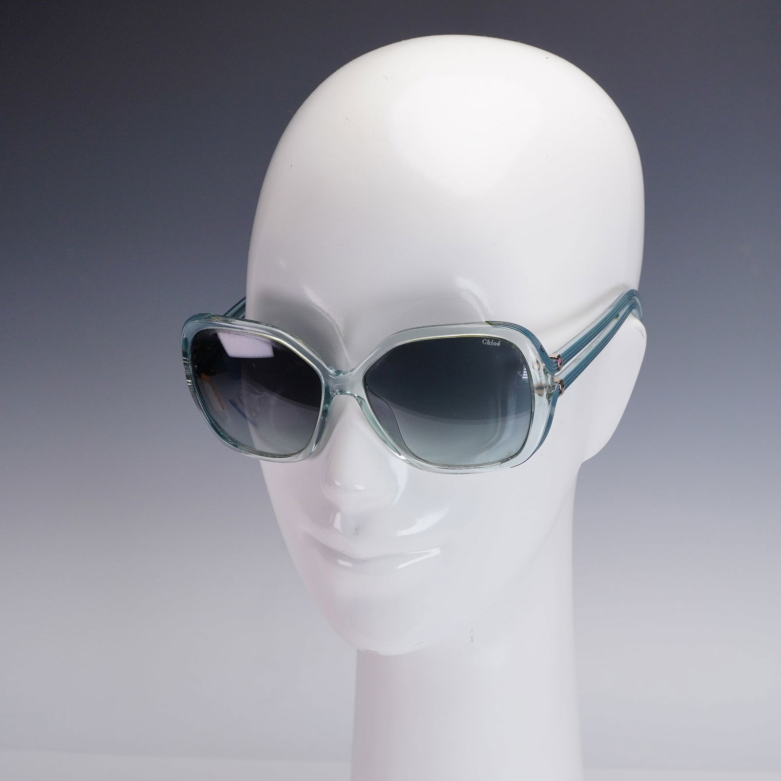 Chloe Oversized Sunglasses in Case: A pair of Chloe oversized sunglasses featuring translucent seafoam green frames and dark gradient lenses. The rounded butterfly shape evokes a bold, retro-inspired silhouette. The Chloe logo is etched