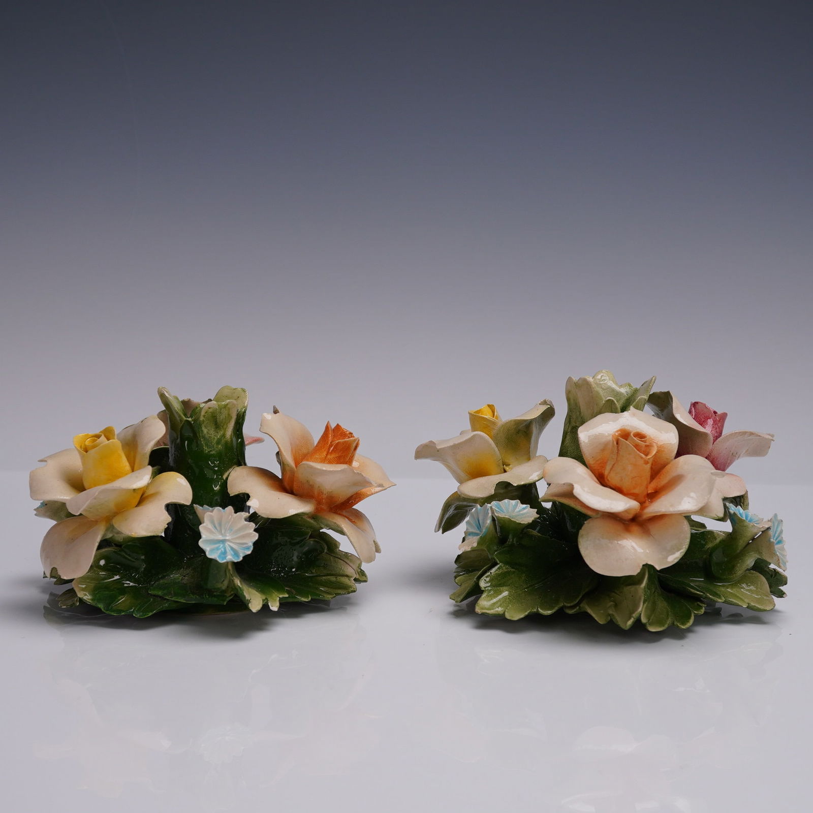 Pair of Capodimonte Style Porcelain Floral Candle Holders: This pair of porcelain floral candle holders includes one marked Capodimonte, while the other is unmarked. Both holders feature intricately crafted blossoms in pastel shades of pink, yellow, blue, and