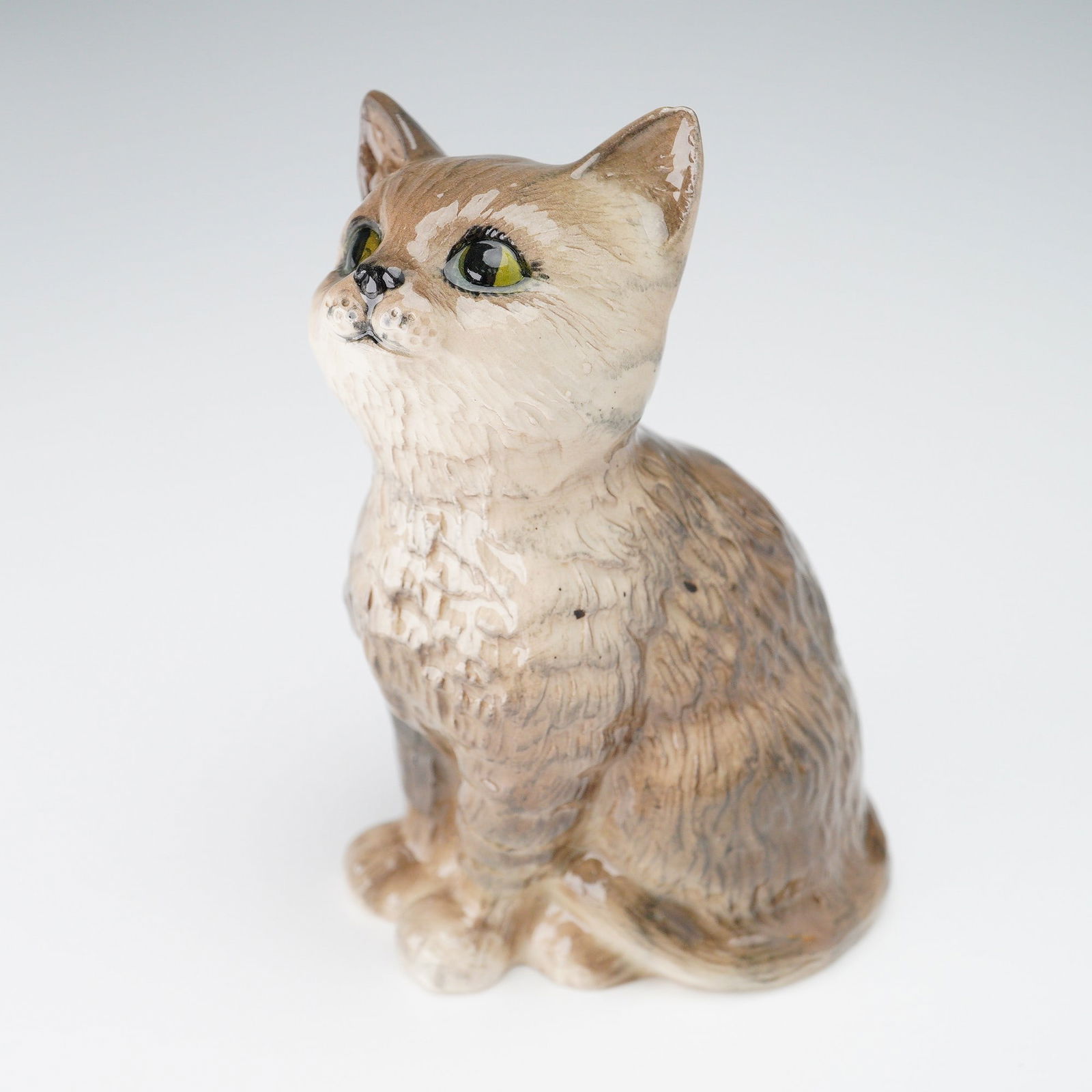 Royal Doulton Porcelain Figurine, Persian Kitten DA128: Cat in a warm beige and gray glaze with finely textured fur and expressive green eyes. The hand painted details emphasize the natural striping and round facial features associated with the breed. The
