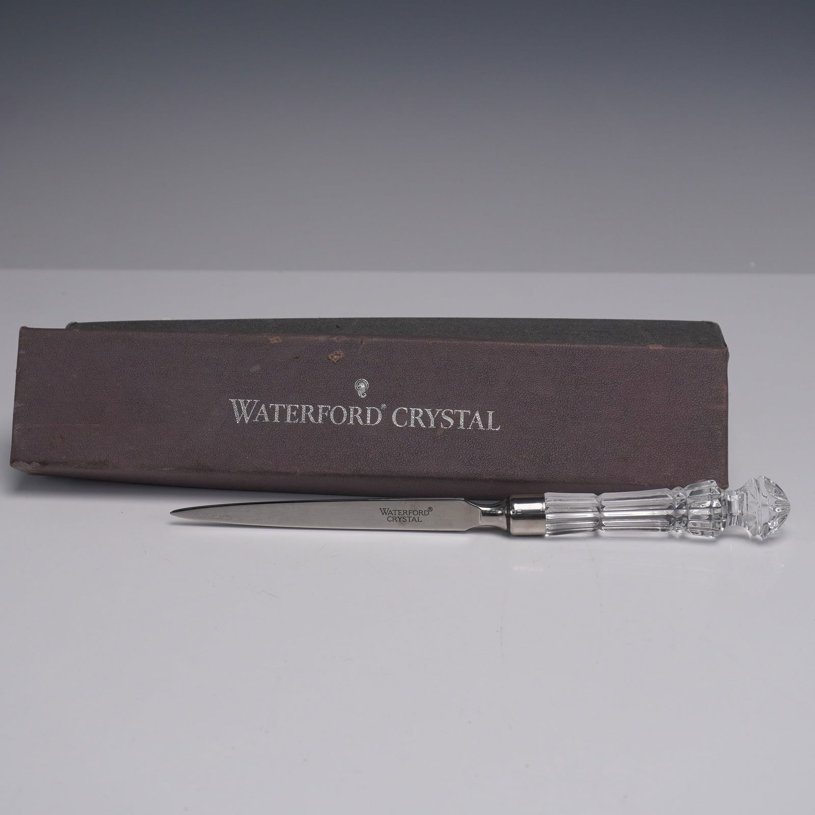 Waterford Crystal Letter Opener With Original Box: Waterford letter opener featuring a faceted crystal handle with fluted and geometric detailing, and a stainless steel blade marked "Waterford Crystal." The blade is tapered to a fine point, ideal for