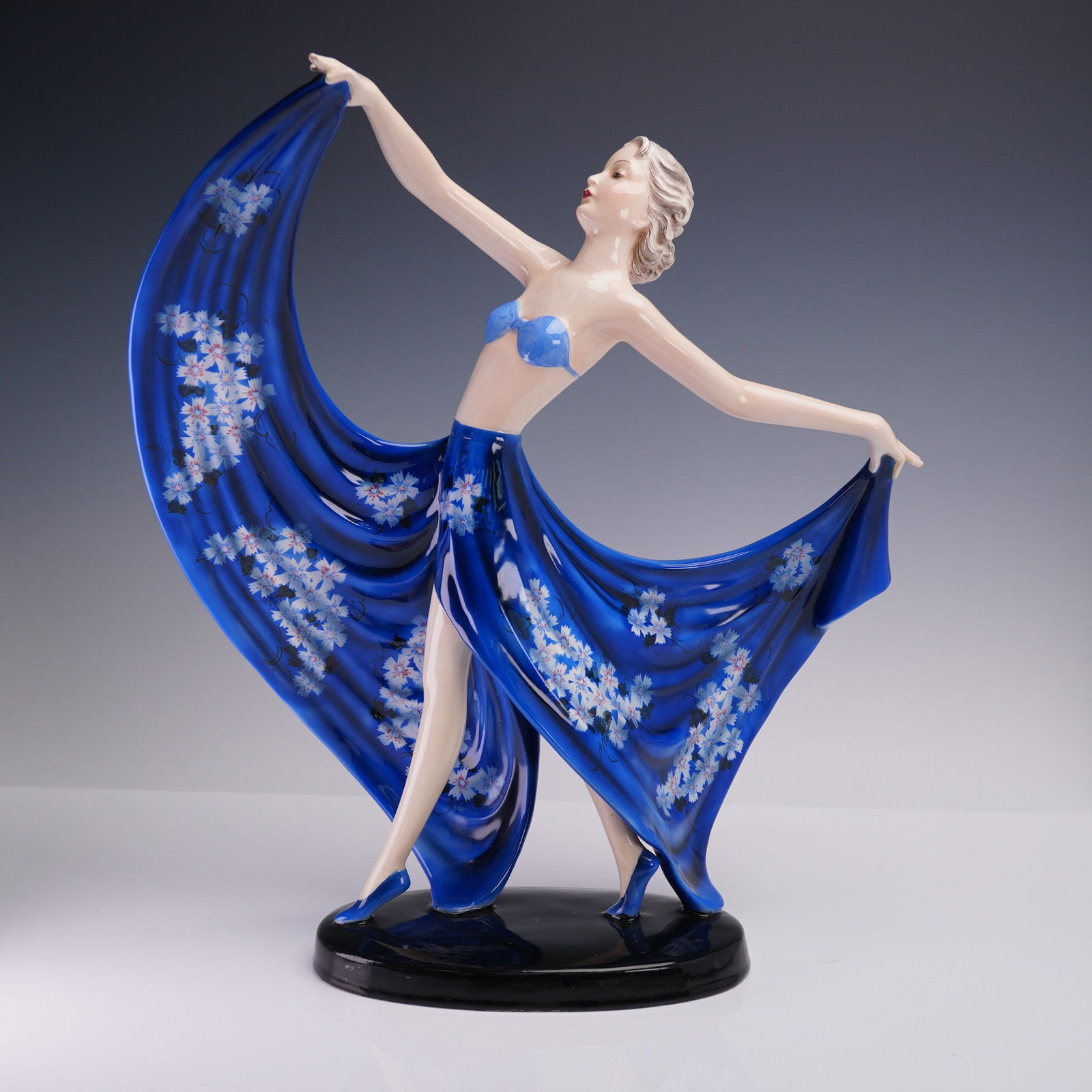 Goldscheider Porcelain by Stefan Dakon Art Deco Dancer Figurine, 7857: Goldscheider porcelain figurine designed by Stefan Dakon, model number 7857, representing a stylized Art Deco dancer. The figure is depicted mid-performance, posed with arms extended outward holding t
