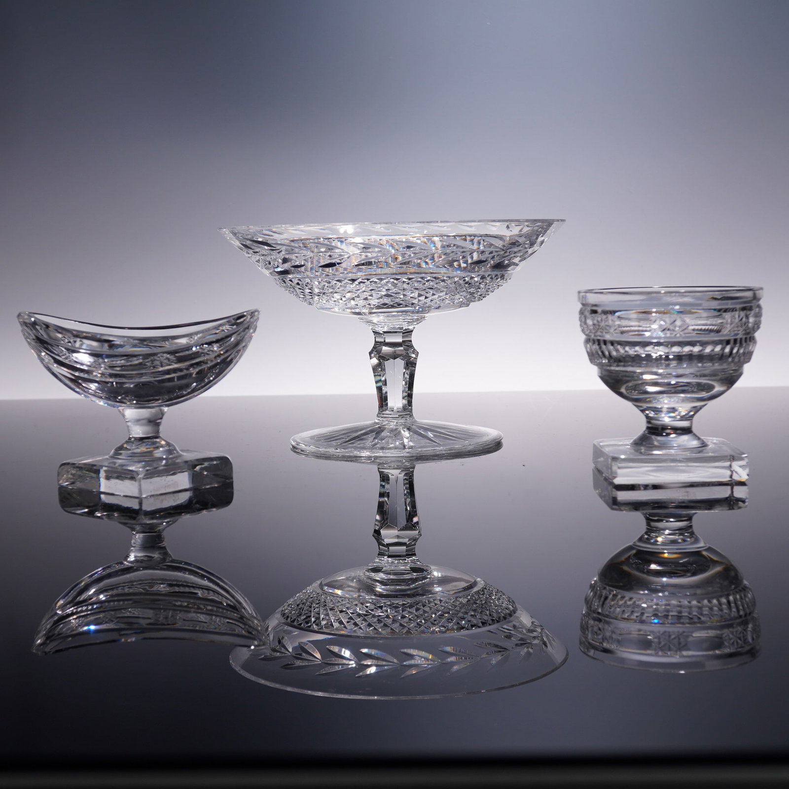 3pc Waterford Crystal Table Accessories: A grouping of three Waterford cut crystal table items, comprising a pedestal compote, a crescent-shaped salt, and a round footed salt. The compote features a deep bowl finely cut with hobstar, diamond