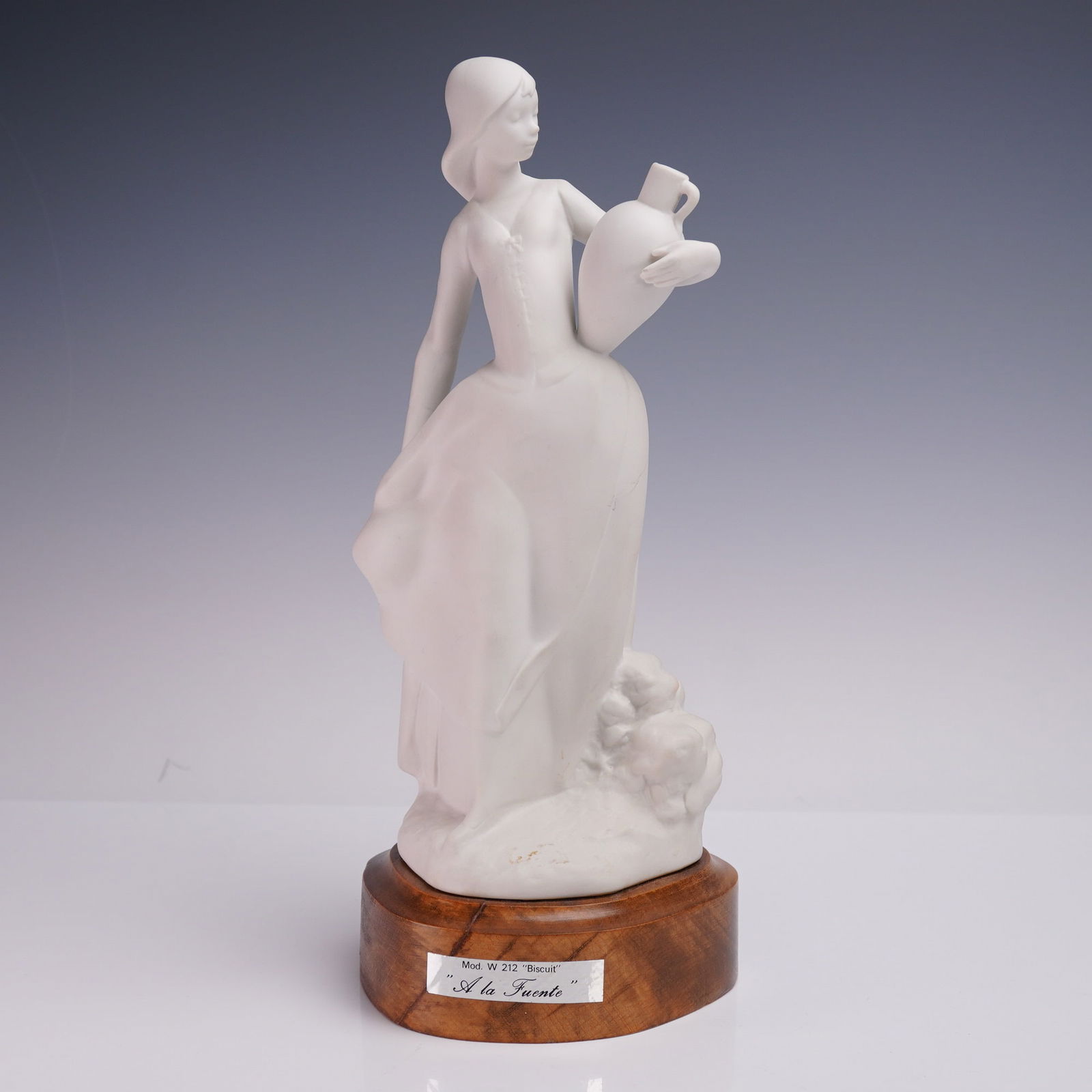 A la Fuente Bisque Porcelain Figurine on Wood Base: Model W 212 bisque porcelain figurine titled A la Fuente, depicting a young woman in a flowing dress carrying a water jug at her side. Rendered in matte white porcelain with softly sculpted detail and