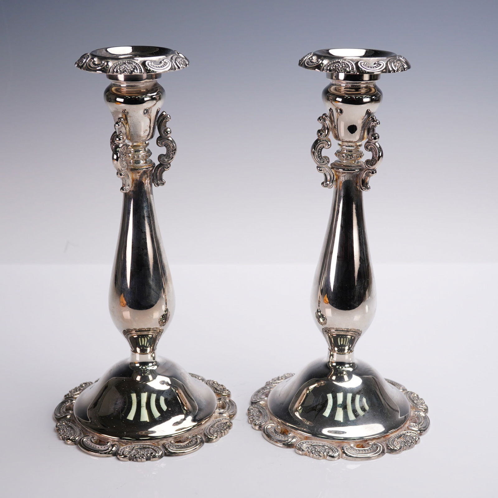 Pair of Wallace Silver Plated Candle Holders: A pair of silver-plated candlesticks by Wallace Silversmiths, designed with elegant elongated baluster forms and scrolled acanthus handles flanking the upper columns. Each rests on a scalloped circula
