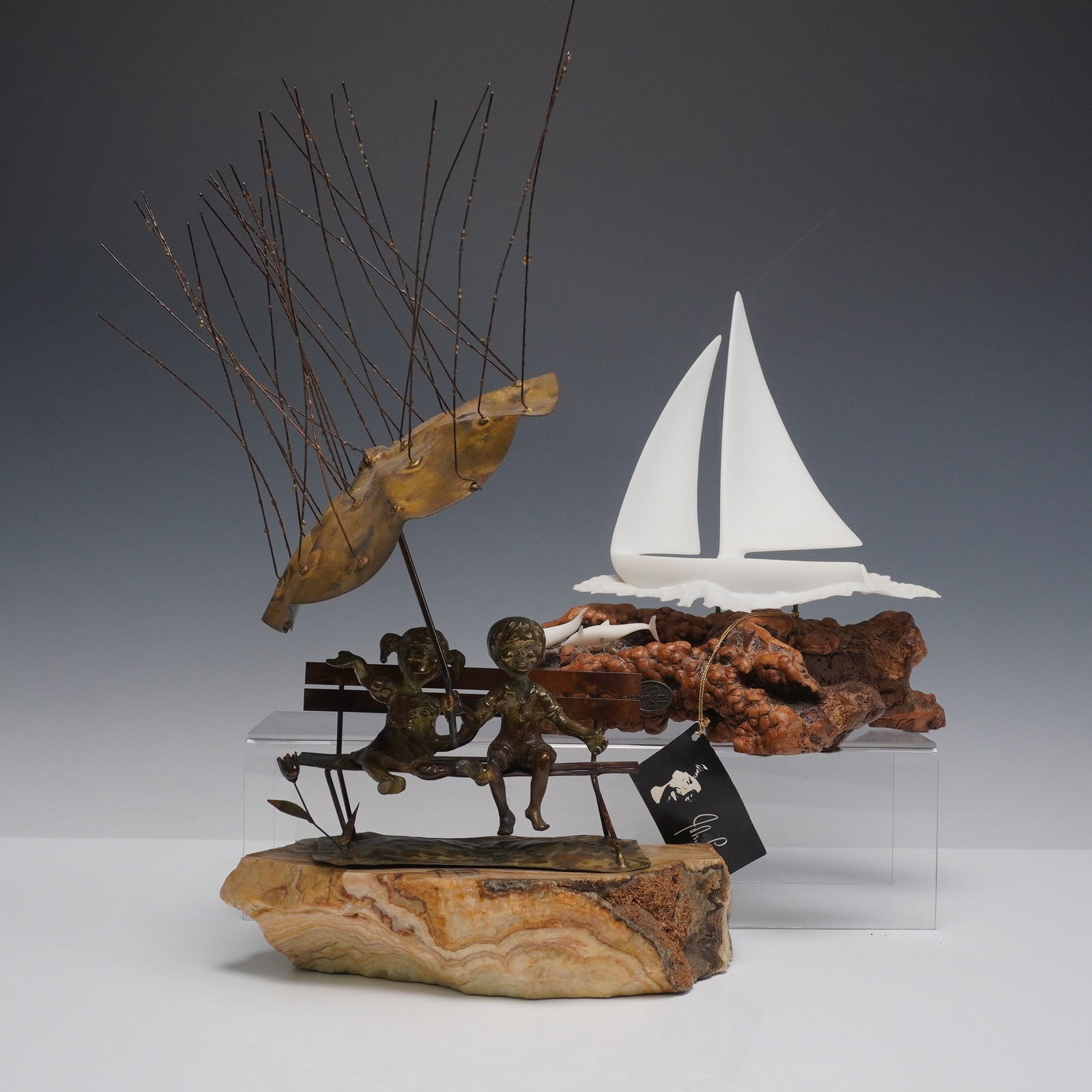 2pc Bronze and Stone Brutalist Sculptures by Bijan Bahar and John Perry: Brutalist mixed media sculptures including a bronze and stone composition by Bijan Bahar depicting two children on a swing beneath a stylized tree canopy, mounted on a natural stone base and signed to