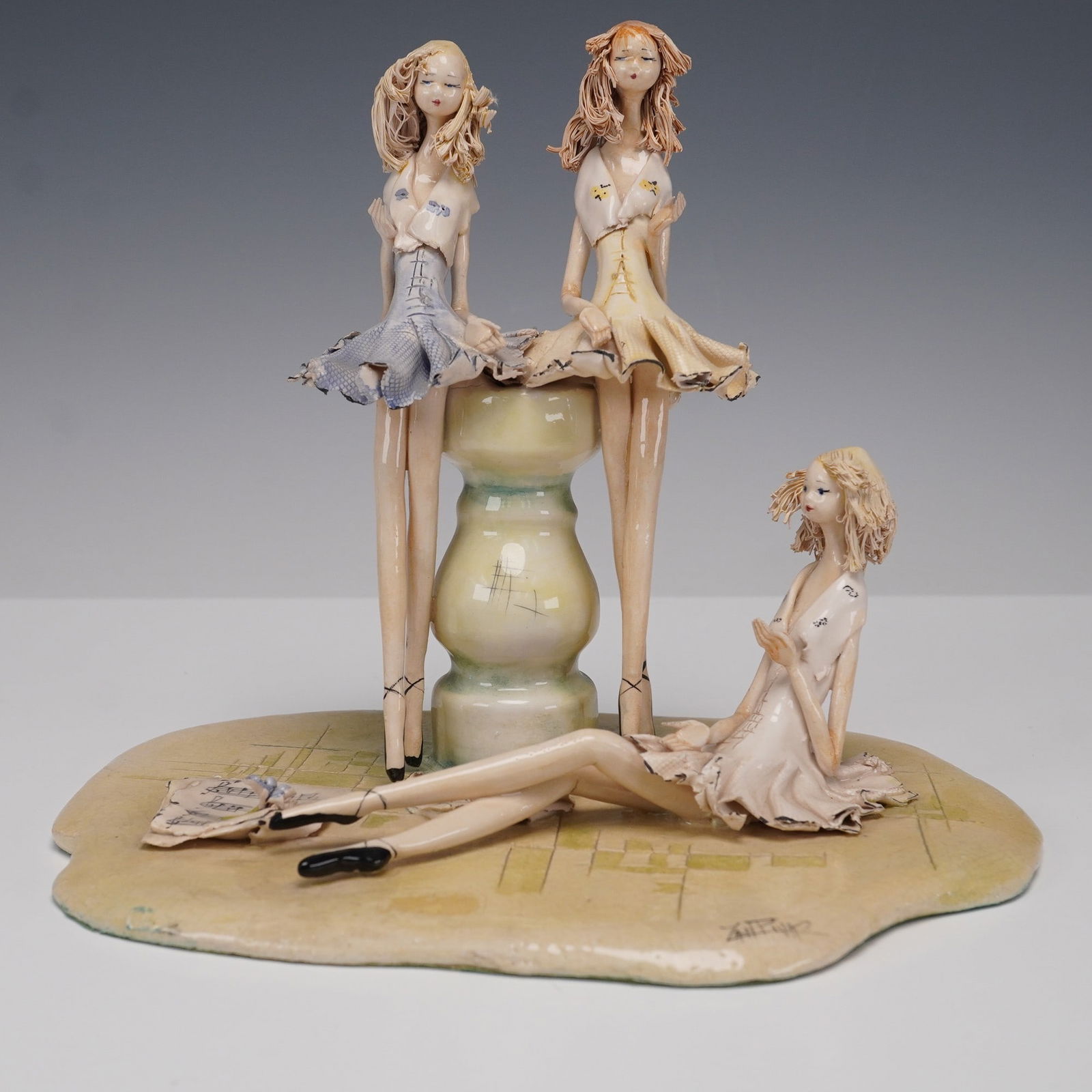 Italian Ceramic Figurine, Ballerinas: Expressive Italian ceramic figurine featuring three stylized ballerinas, two perched atop a rounded pedestal and one reclining gracefully at the base. Each dancer is depicted in a short flared dress w