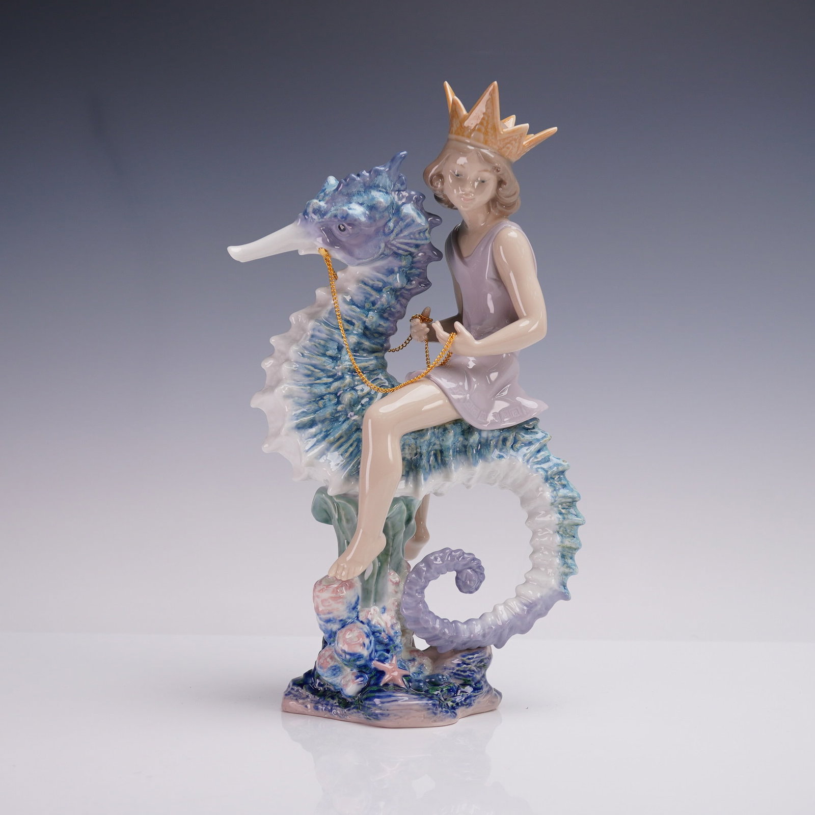 Lladro Porcelain Figurine, Prince of the Sea 1001821: The figure depicts a youthful crowned figure seated side-saddle atop a large stylized seahorse, rendered in soft pastel tones with high-gloss finish. The seahorse is sculpted in shades of blue, purple