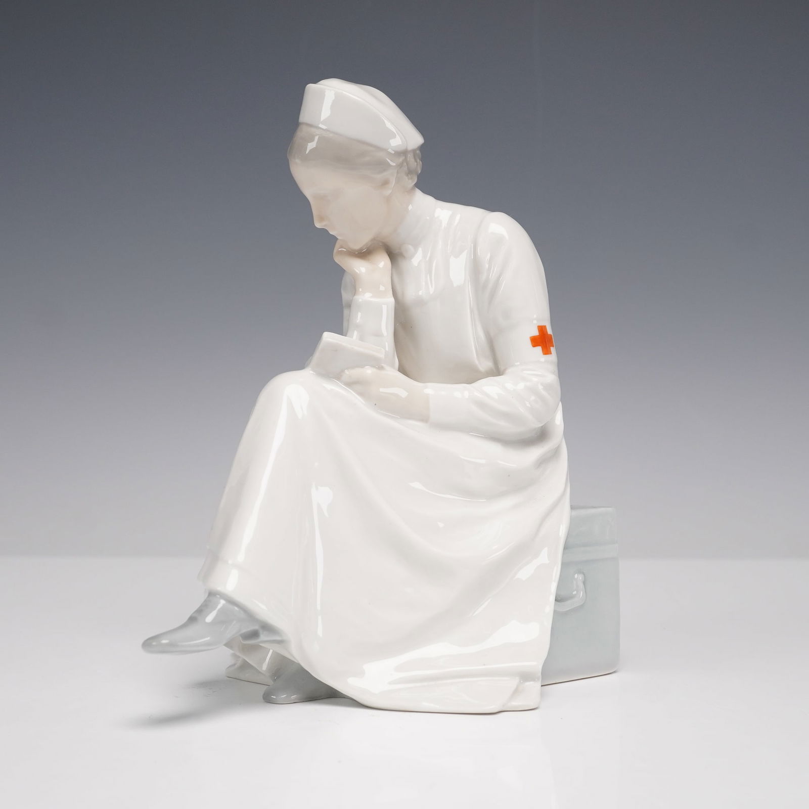 Bing & Grondahl Porcelain Red Cross Nurse Figurine 1866: A porcelain figurine by Bing & Grondahl of Denmark, model number 1866, depicting a seated Red Cross nurse in uniform with a thoughtful expression as she reads a letter. The figure is rendered in gloss