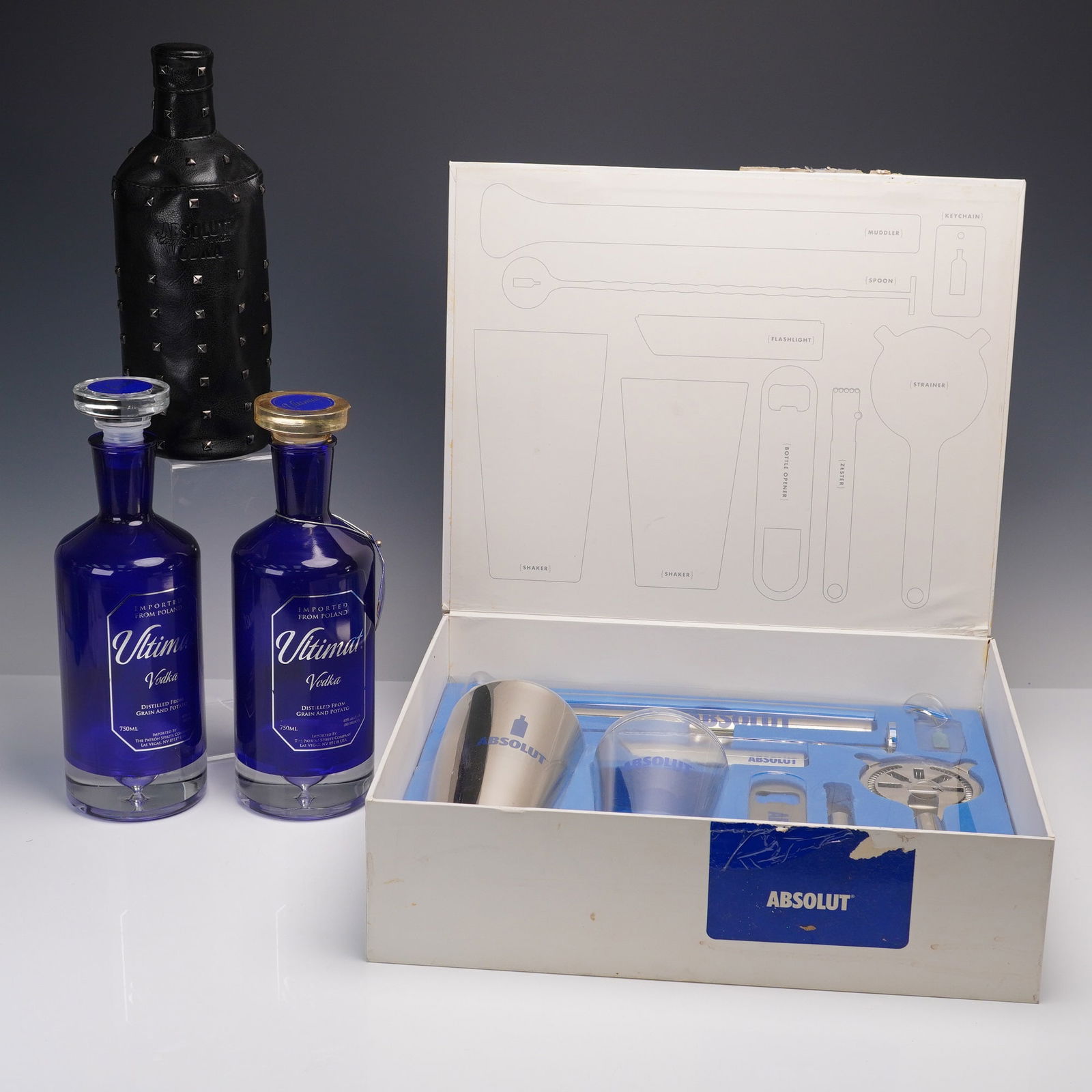 4pc Ultimat & Absolut Vodka Collectors' Set with Bar Tools & Limited Bottle: A four-piece collector's grouping featuring two cobalt blue Ultimat Vodka bottles (750ml, empty), one Absolut Vodka bottle in a studded black leather zip-up case marked Country of Sweden, and one boxe