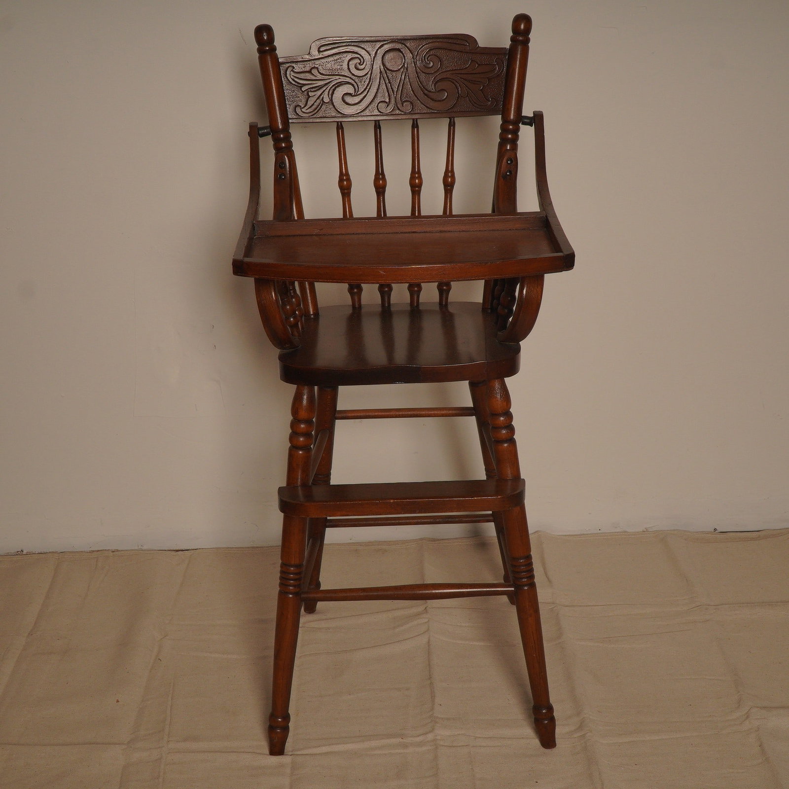 Vintage Wooden High Chair with Carved Back and Lift-Front Tray: This vintage wooden high chair showcases classic craftsmanship with a warm, medium-brown finish and beautifully turned legs. The highlight of the design is the ornately carved backrest, featuring an i