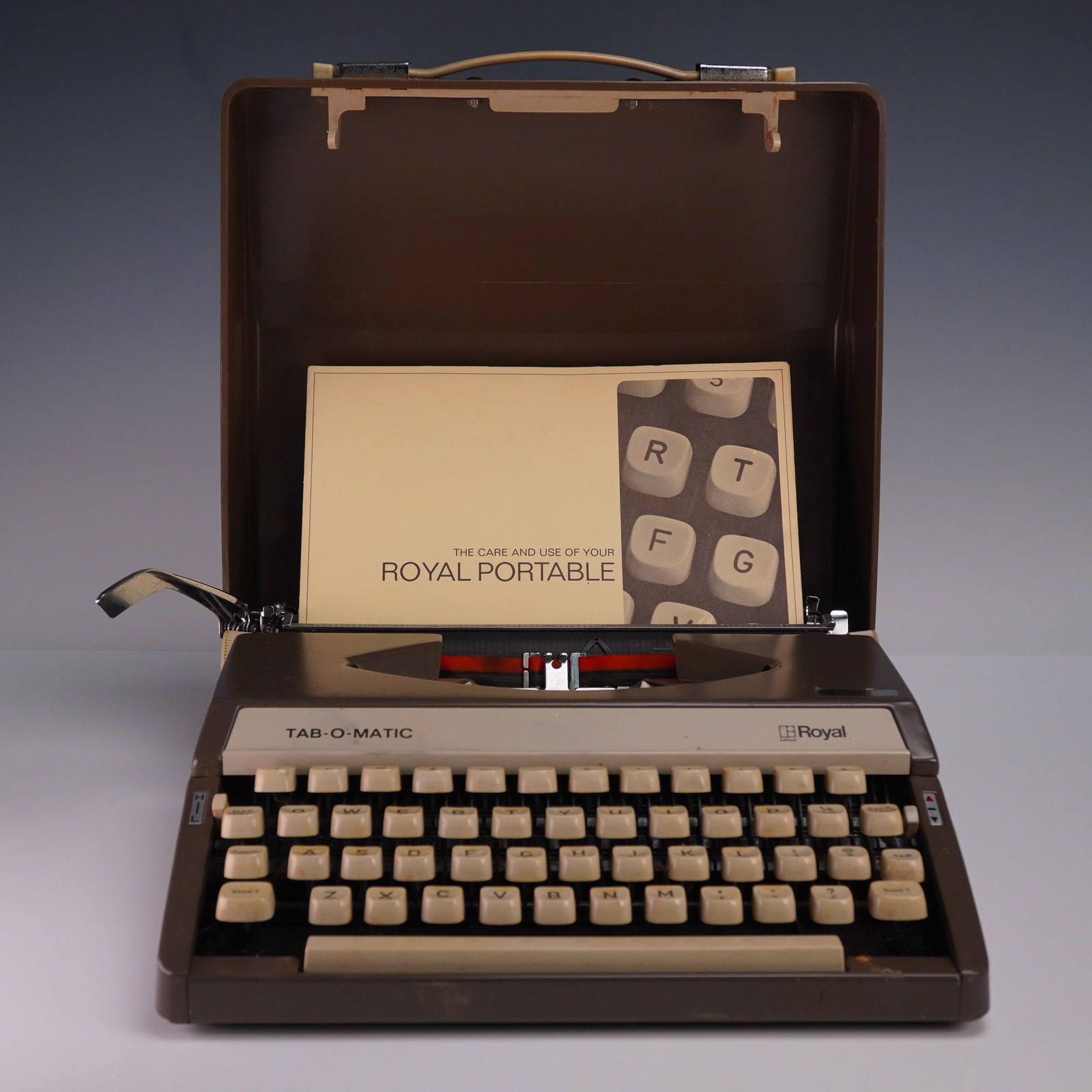 Royal Tab-O-Matic Portable Typewriter with Case and Manual: Vintage Royal Tab-O-Matic portable typewriter in brown and beige finish, housed in its original fitted hard plastic carrying case with metal latches and molded plastic handle. This mid-century mechani