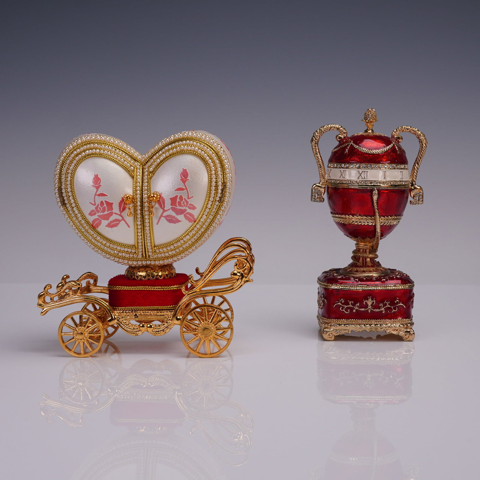 Pair of Jeweled Musical Trinket Boxes, Heart Coach & Urn Clock Form: A whimsical pair of jeweled musical trinket boxes. The first features a heart-shaped hinged coach design with twin doors decorated in red roses, beaded trim, and ornate gold-tone metal carriage wheels