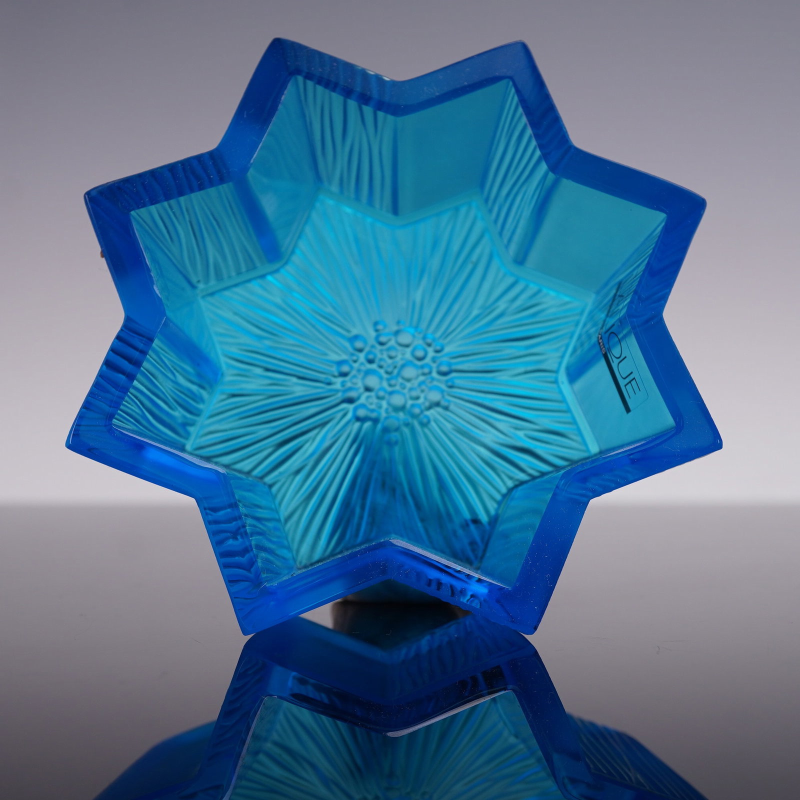 Lalique Crystal Star Bowl, Antares Dark Blue: A vivid blue crystal bowl in the shape of a star with crisp angular edges and vertical ribbed paneling along the exterior. Lalique sticker label. Lalique etched backstamp. This item has its original b