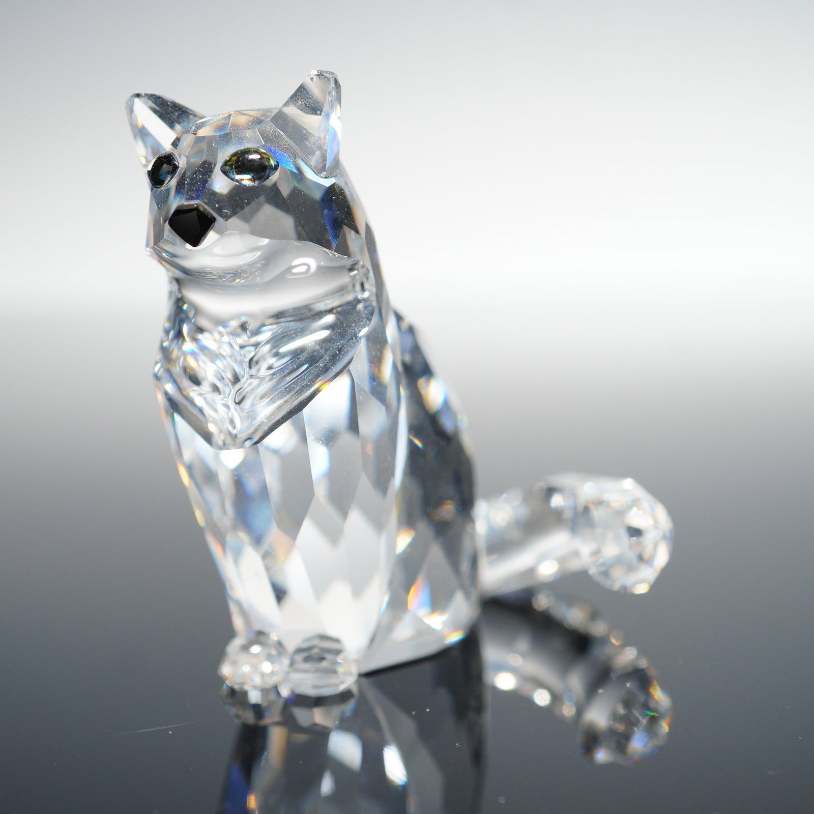 Swarovski Crystal Figurine, Cat Sitting 160799: Clear crystal figurine depicting a seated cat with faceted body, jet crystal eyes, and nose. Features the Swarovski swan logo laser-etched on the base. Includes original navy cylindrical box packaging
