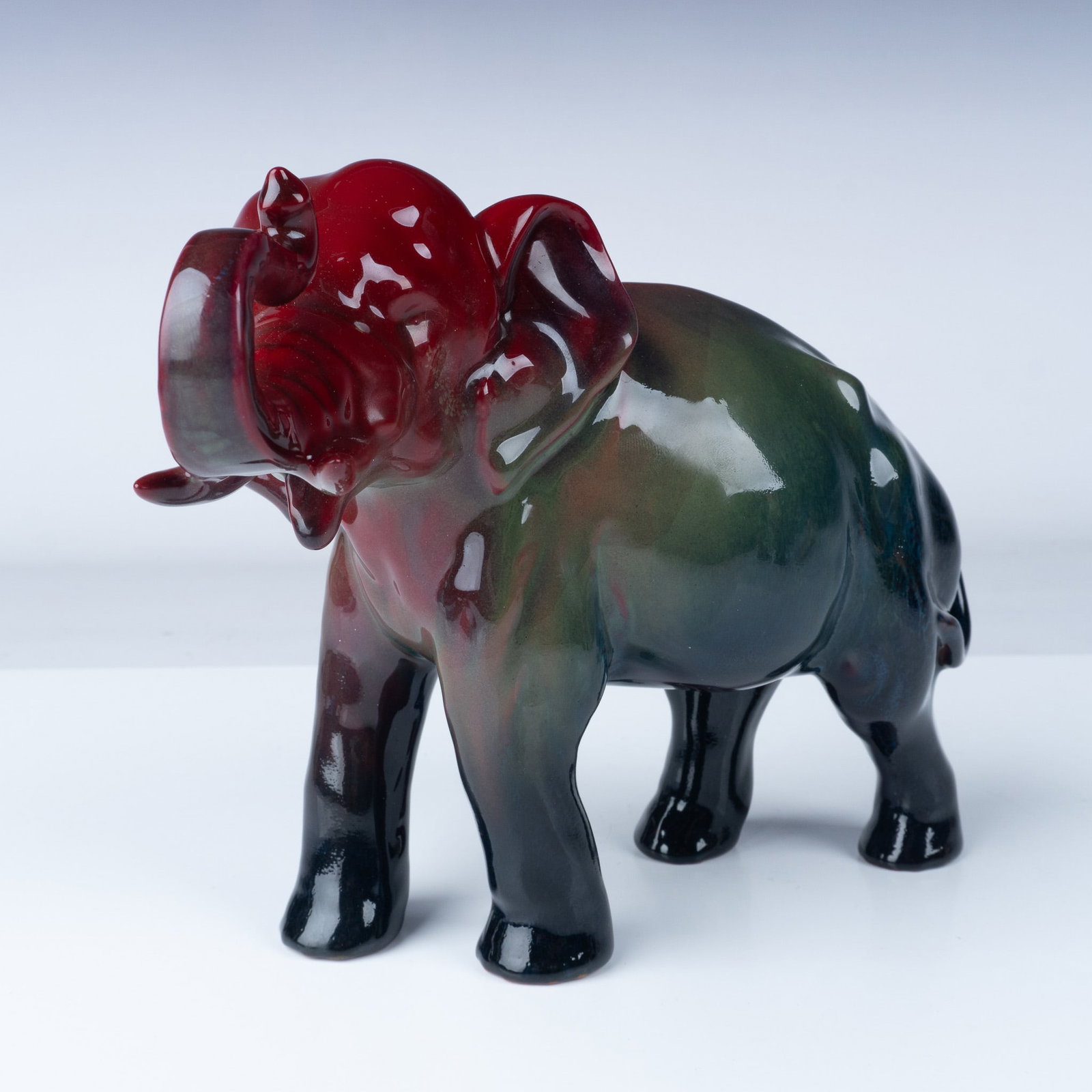 Royal Doulton Flambe Sung Figurine, Elephant HN966: Elephant - Trunk In Salute. A striking Royal Doulton Flambe Sung elephant figurine, showcasing the brand's signature high-gloss glaze with deep red and black tones blending seamlessly across the form.