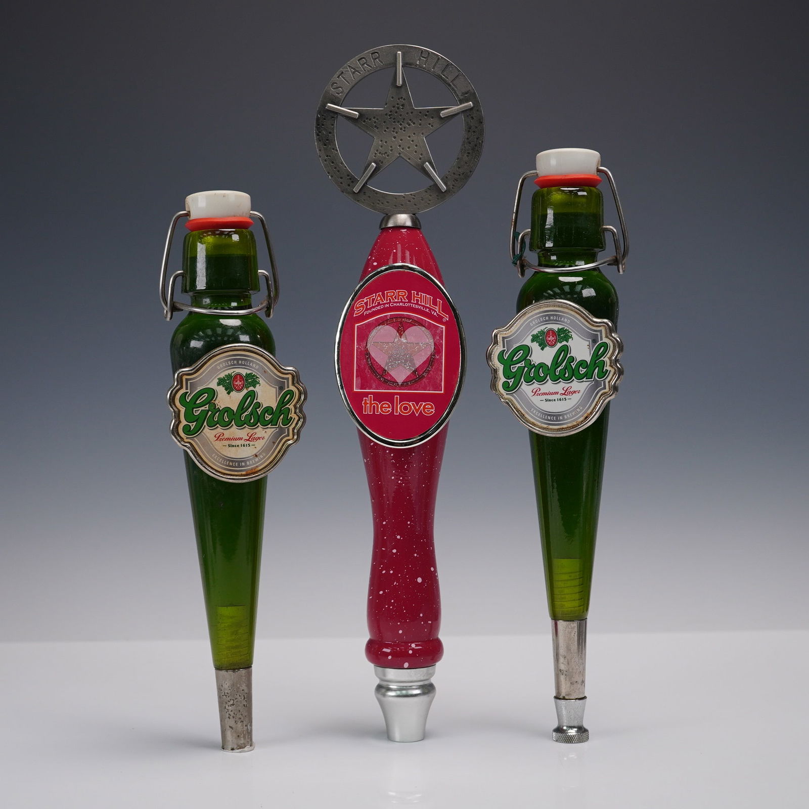 3pc Grolsch & Starr Hill Beer Tap Handles: Set of three beer tap handles including two matching Grolsch Premium Lager taps styled like miniature green swing-top bottles, and one Starr Hill "The Love" handle in red with a prominent star topper
