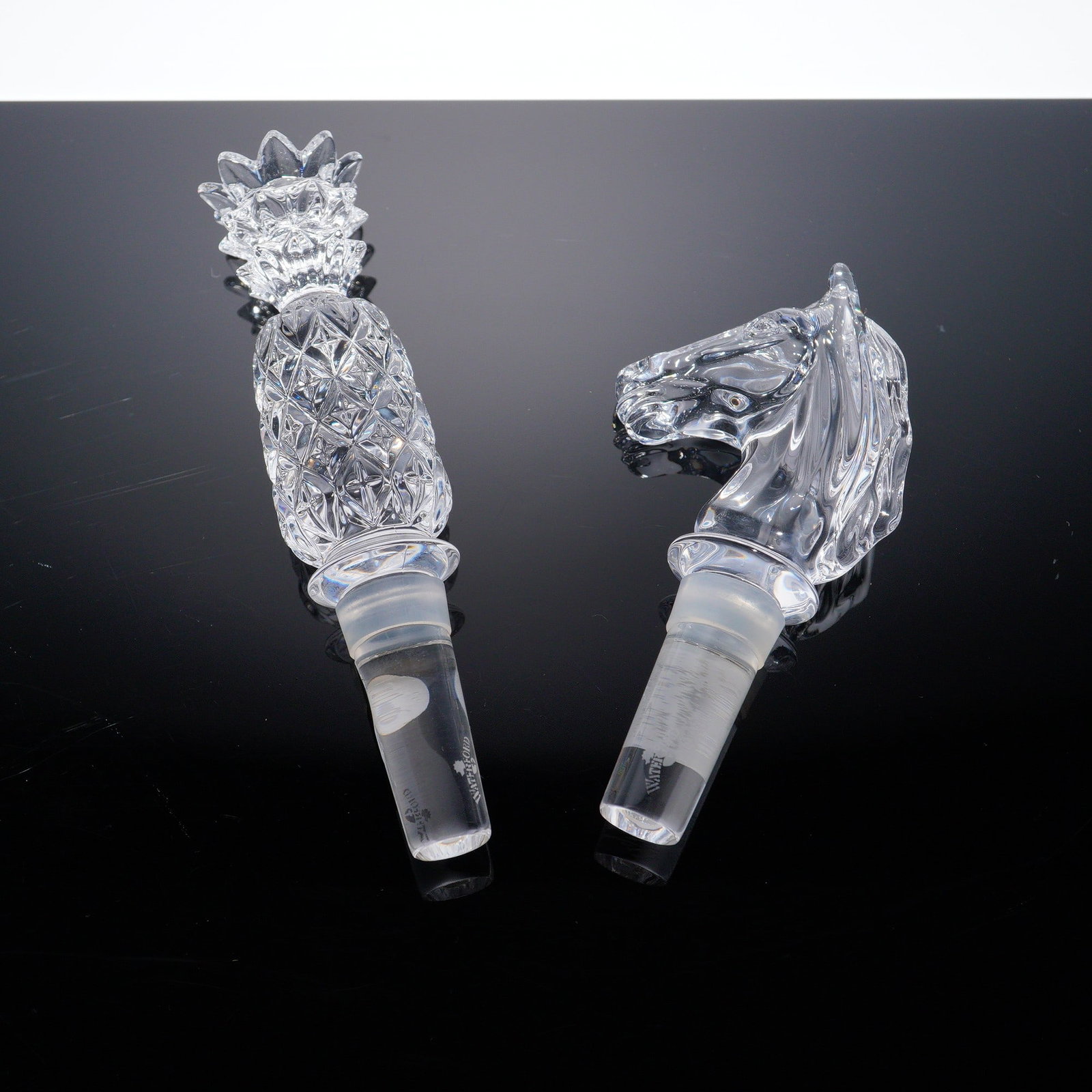 Pair of Waterford Crystal Bottle Stoppers, Pineapple and Horse Designs: Pair of Waterford crystal bottle stoppers featuring sculptural finials in pineapple and horse head forms. The pineapple stopper displays intricate crosscut facets while the horse head is gracefully mo