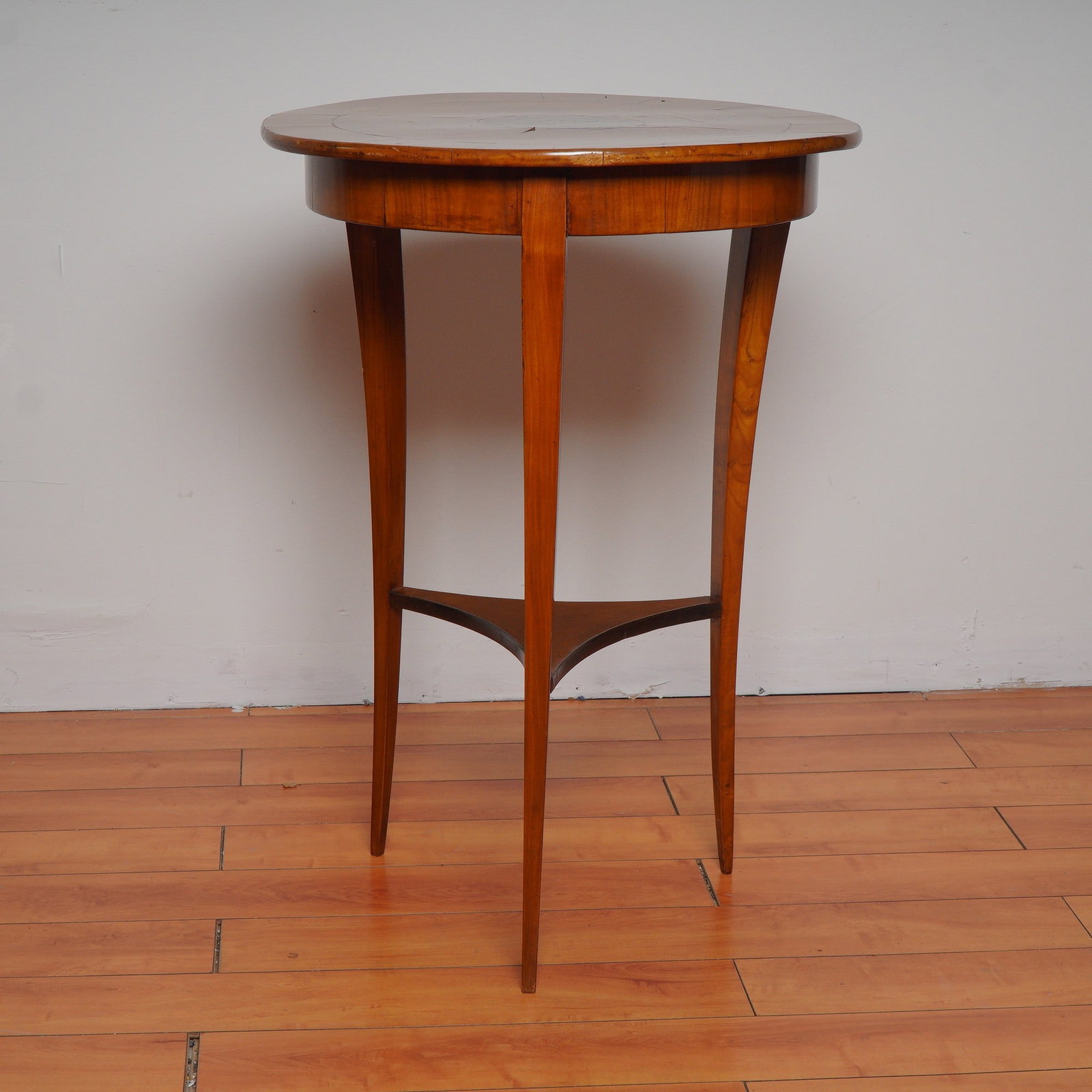 Vintage Round Inlaid Wood Accent Table with Tapered Legs: Graceful vintage side table featuring a round veneered top with radial wood grain and a central inlaid medallion. Supported by slender tapered legs joined by a curved stretcher, this piece showcases r