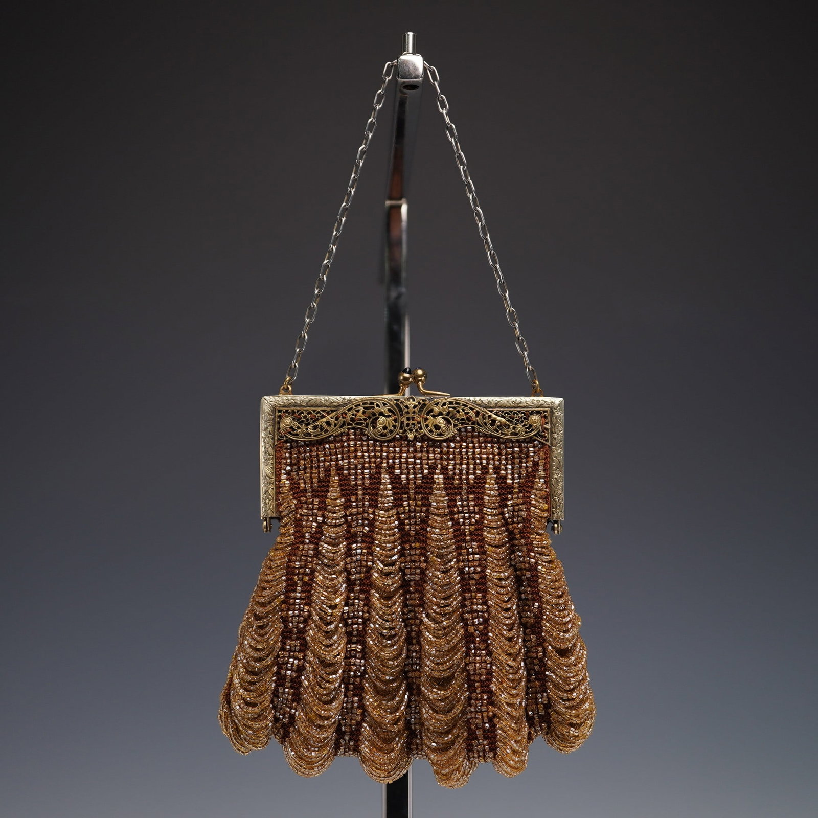 Art Nouveau Beaded Evening Handbag: This striking Art Nouveau handbag features amber glass beads arranged in elegant scalloped rows over a brown crocheted base. The hinged frame presents intricate openwork filigree, floral engraving, an