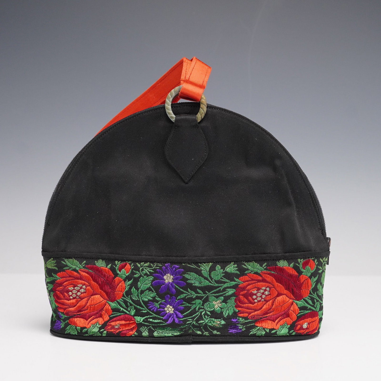 Renaud Pellegrino Floral Embroidered Black Purse: Striking designer handbag by Renaud Pellegrino, Paris, crafted with a structured black textile body and richly embroidered floral band in bold red, purple, and green. A wide red orange satin strap is 