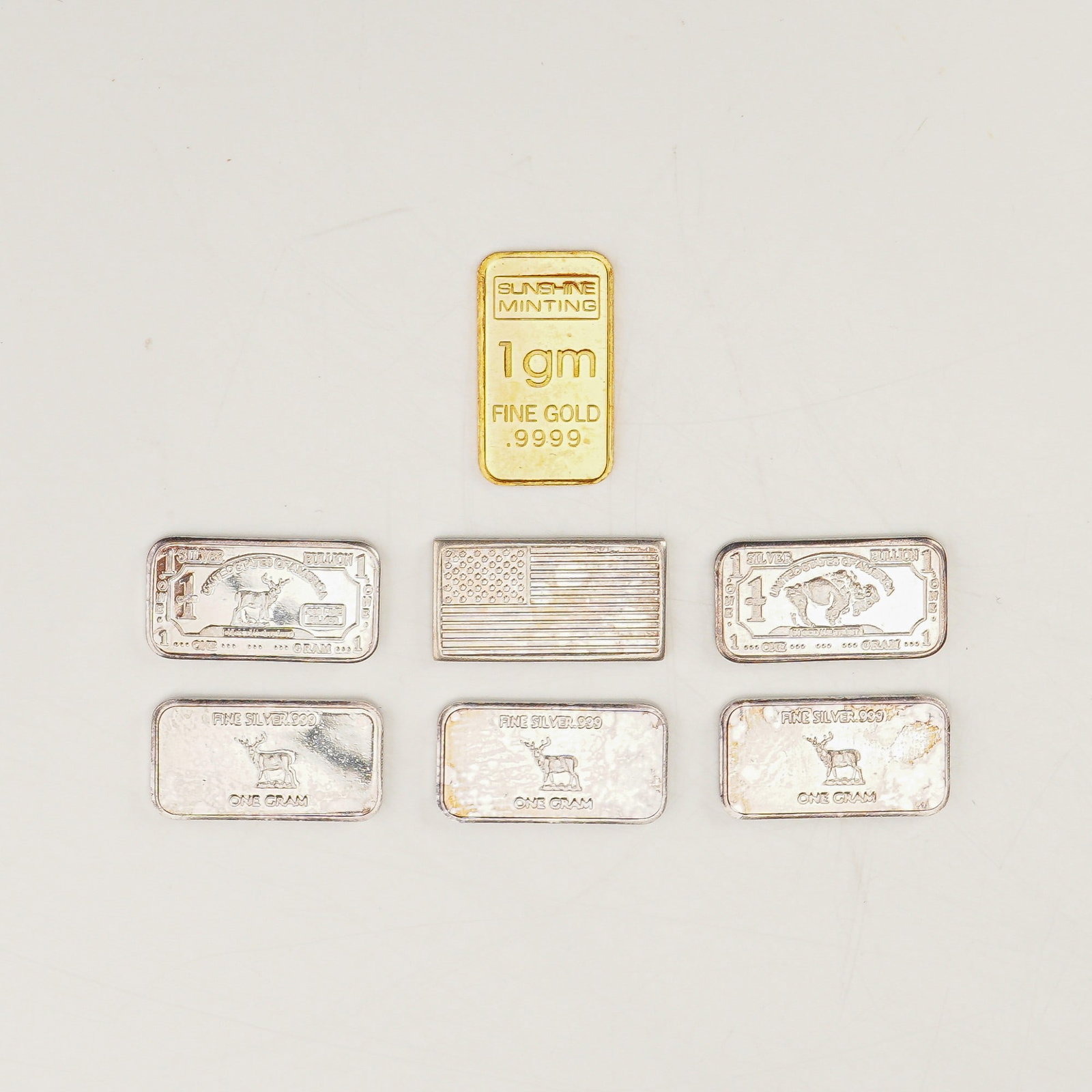 7pc Miniature 1g Silver and Gold Bullion Bars: A total of seven precious metal bullion pieces, including one gold and six silver bars, each weighing one gram. The gold bar is minted by Sunshine Minting and is marked 1gm FINE GOLD .999, showcasing 