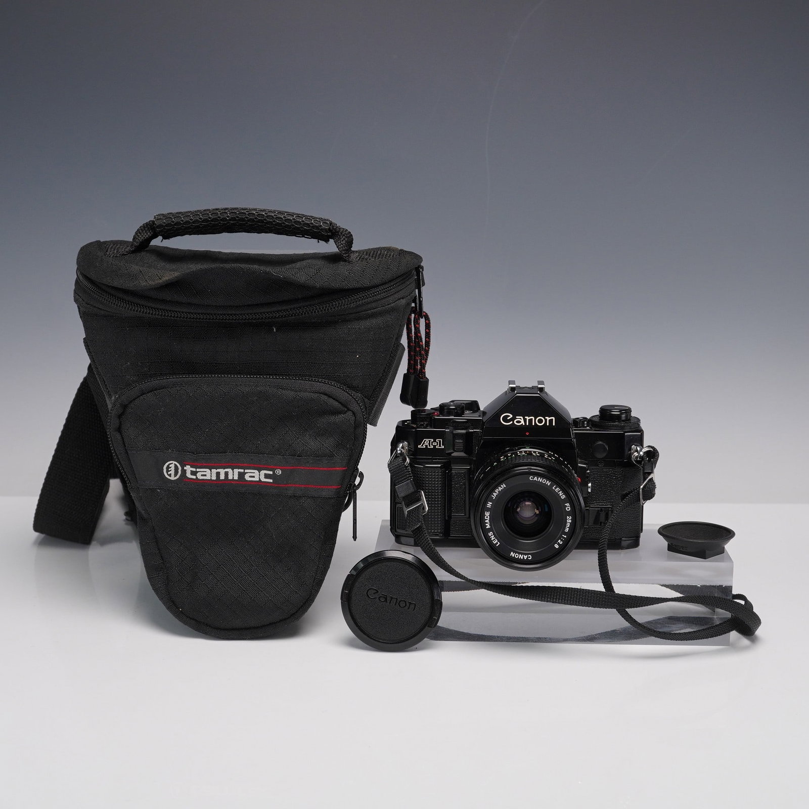 2pc Canon A-1 35mm SLR Film Camera with 28mm Lens and Bag: Canon A-1 35mm SLR film camera fitted with a Canon Lens FD 28mm 1:2.8, featuring black body finish, manual and automatic exposure modes, and original Canon front lens cap. Serial number 682201. Includ
