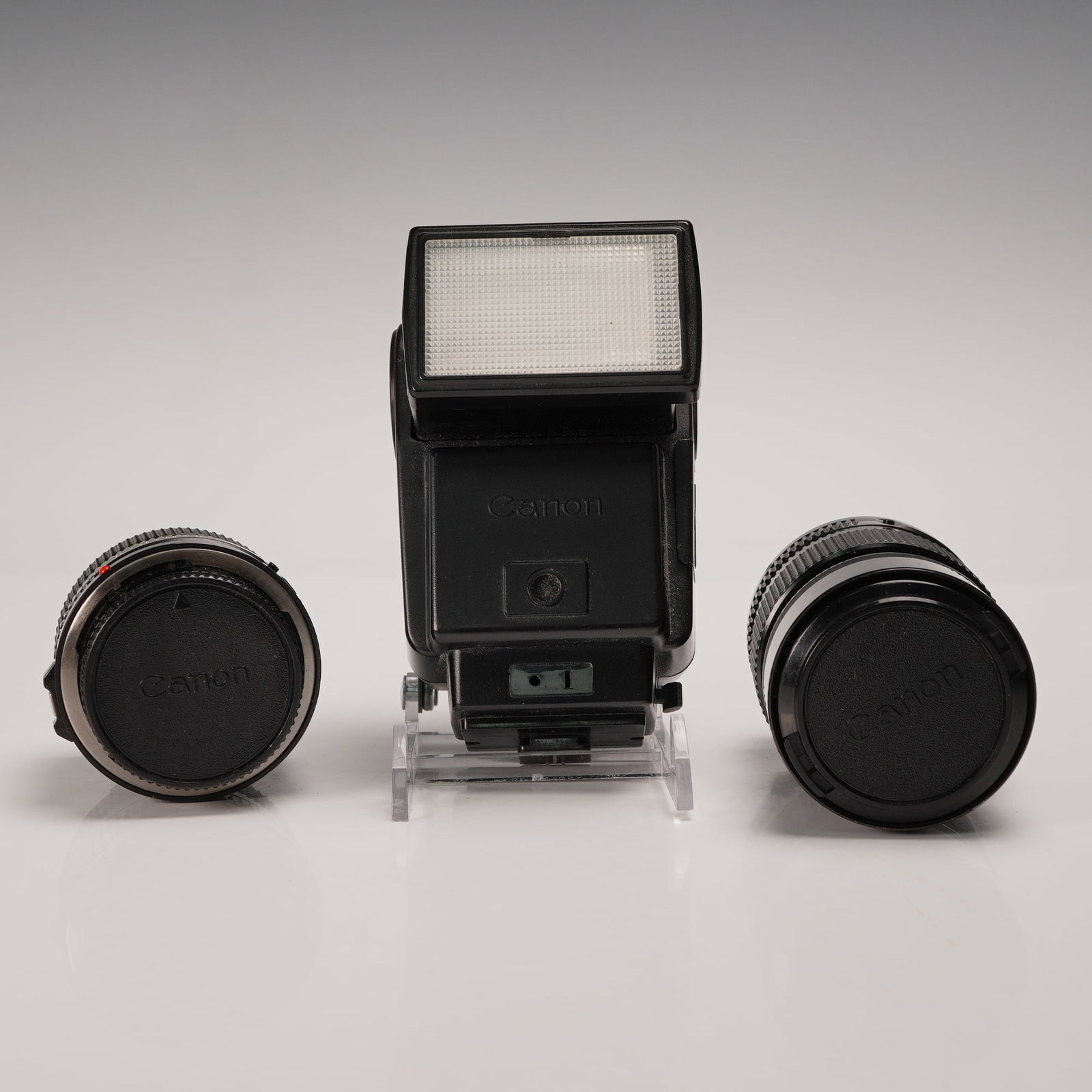 3pc Canon Speedlite 199A Flash with 50mm and 135mm FD Lenses: A three-piece vintage Canon camera accessory lot including two FD mount lenses and a matching Canon Speedlite flash. The lot features a Canon FD 50mm f/1.8 prime lens with 52mm SKY 1-A filter (made in