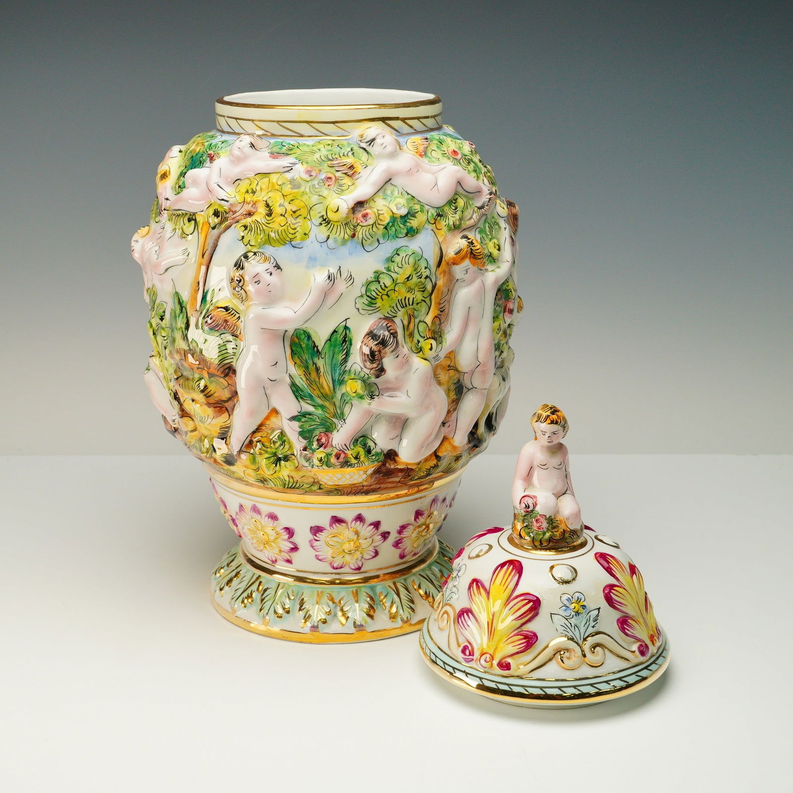 Capodimonte Italian Porcelain Covered Vase with Cherubs: A vibrantly modeled Capodimonte porcelain covered urn, standing 18 inches high, featuring lavish hand-applied cherubs in high relief. Made in Italy and marked Capodimonte 429, the urn is crafted in a