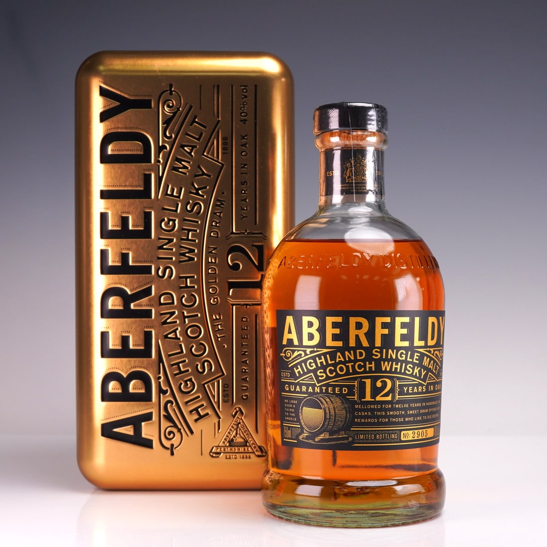Aberfeldy 12 Years Old, Highland Single Malt Scotch Whisky: A bottle of Aberfeldy Highland Single Malt Scotch Whisky, aged 12 years, presented in a striking gold metal gift tin embossed with branding and decorative detail. The whisky is crafted in Scotland and